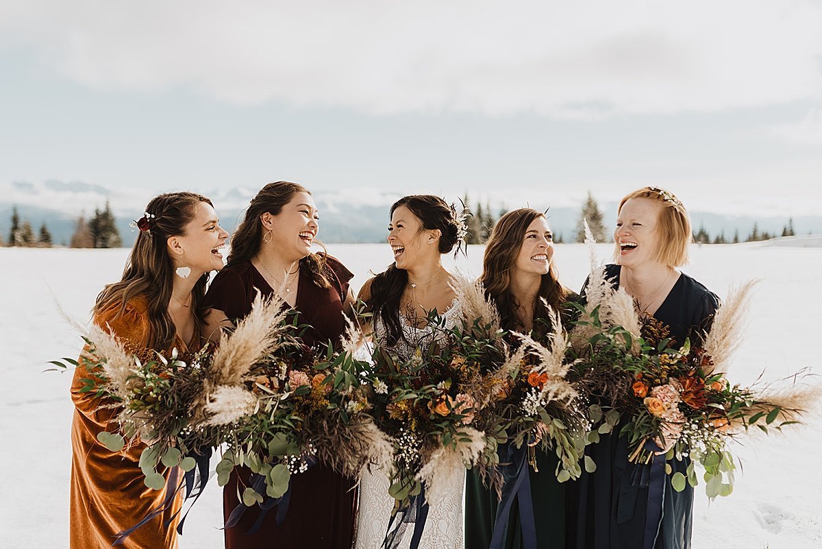  bridal party in warm autumn velvet dresses pose with bride holding fall bouquets at ceremony shot by alaska wedding photographer 