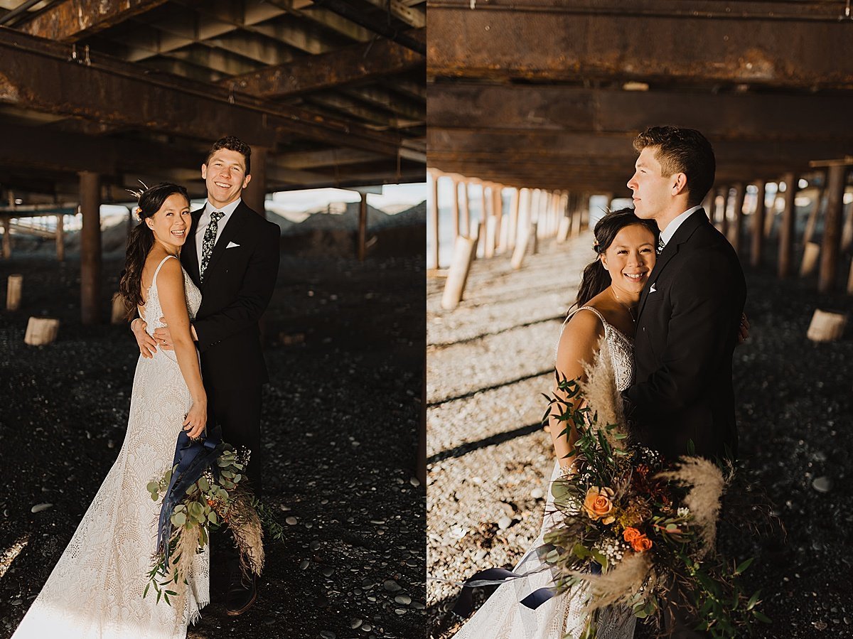  bride with autumn floral bouquet poses with groom under pier at mountain lake shot by alaska wedding photographer 