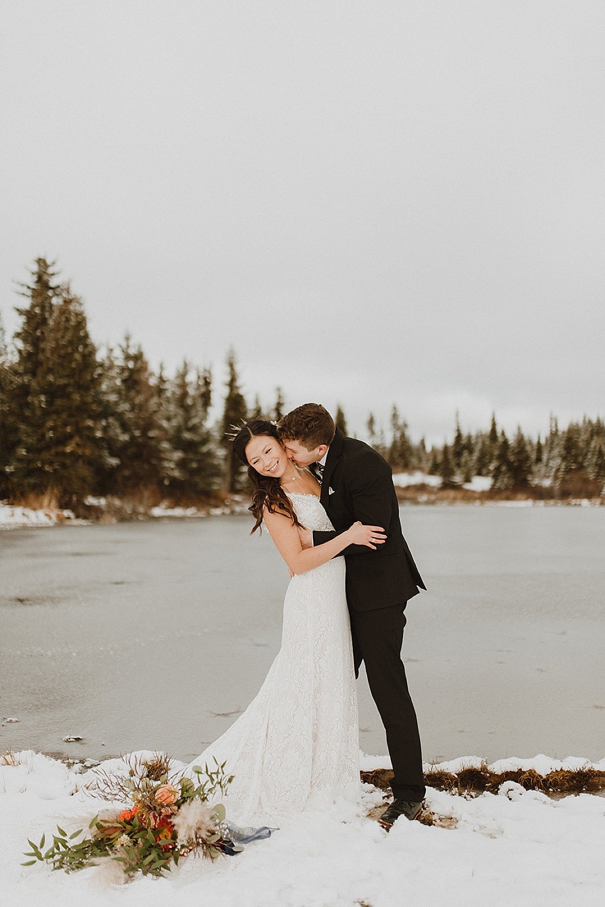  bride and groom kiss beside snowy lake at ceremony shot by alaska wedding photographer 