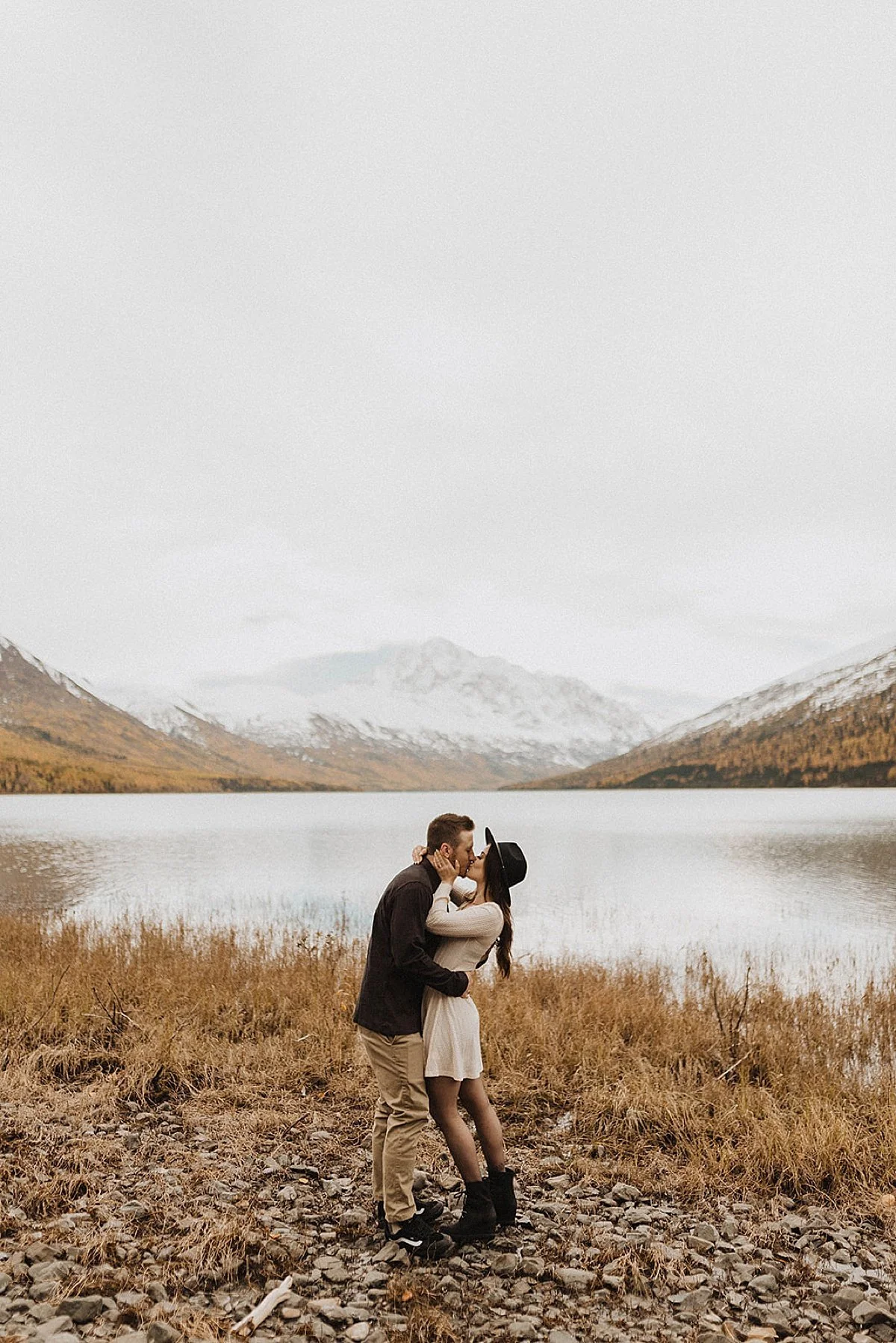 Engaged couple kiss at alaska mountain lake during autumn engagement shoot