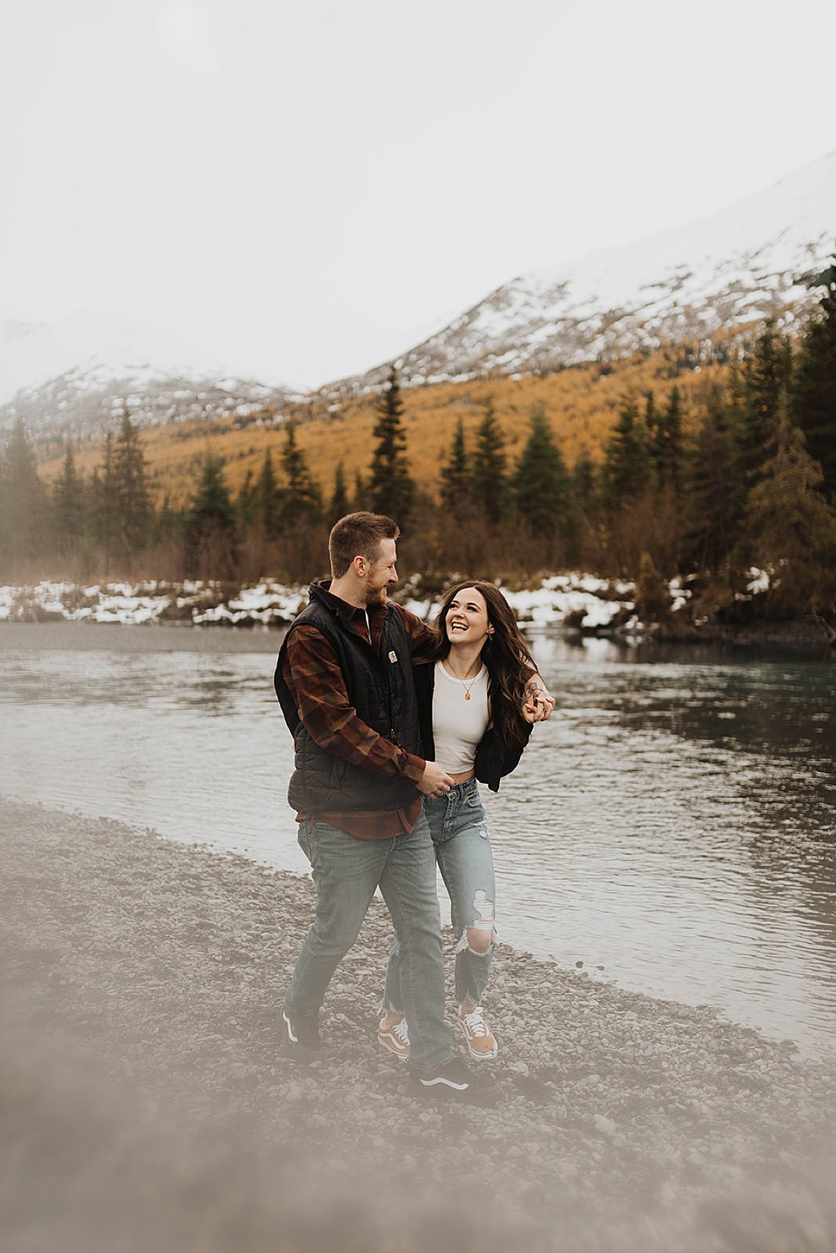  outdoorsy couple in plaid flannel shirts walk along mountain lake beach in engagement session by theresa mcdonald photography 