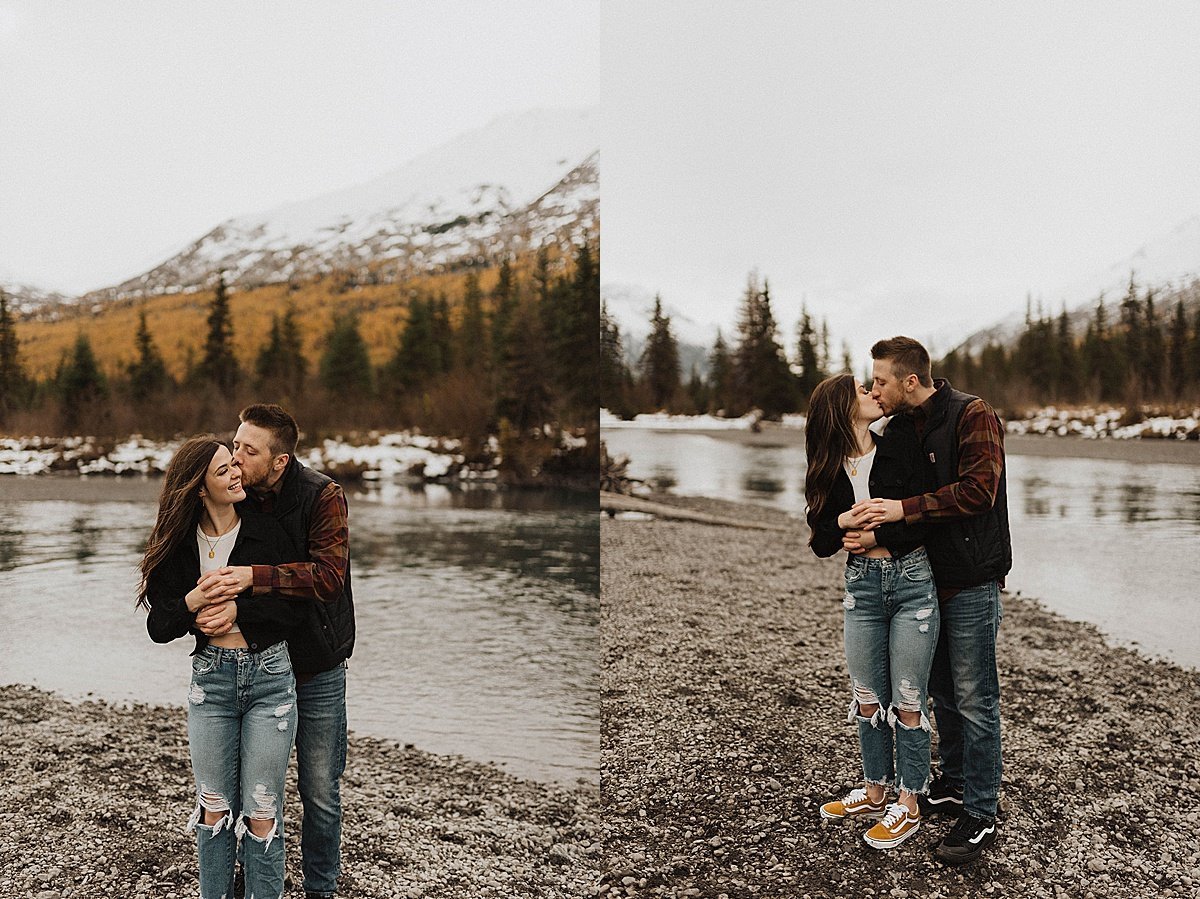  couple in jeans and flannel kiss at rugged mountain lake during autumn engagement shoot by alaska wedding photographer 