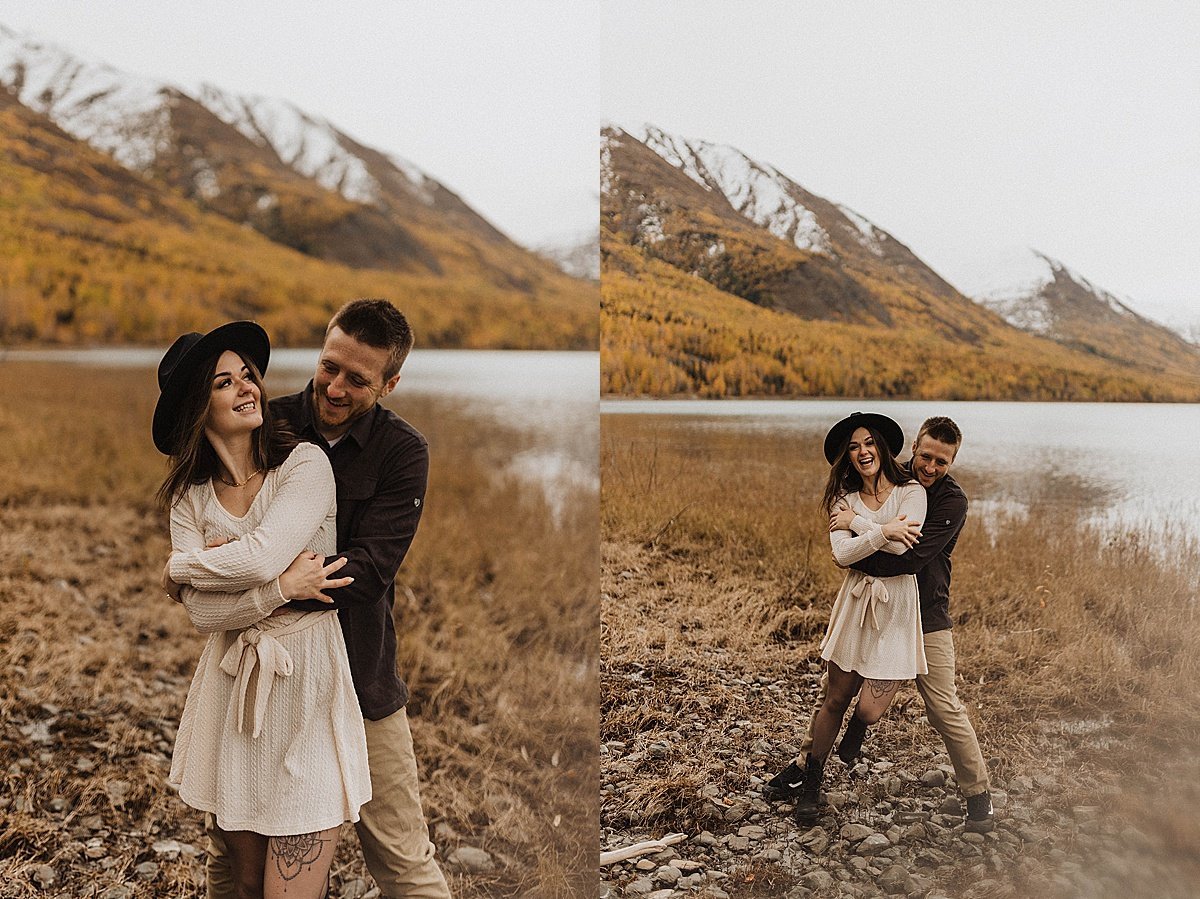  couple laugh in front of mountain lake beach during autumn engagement shoot 