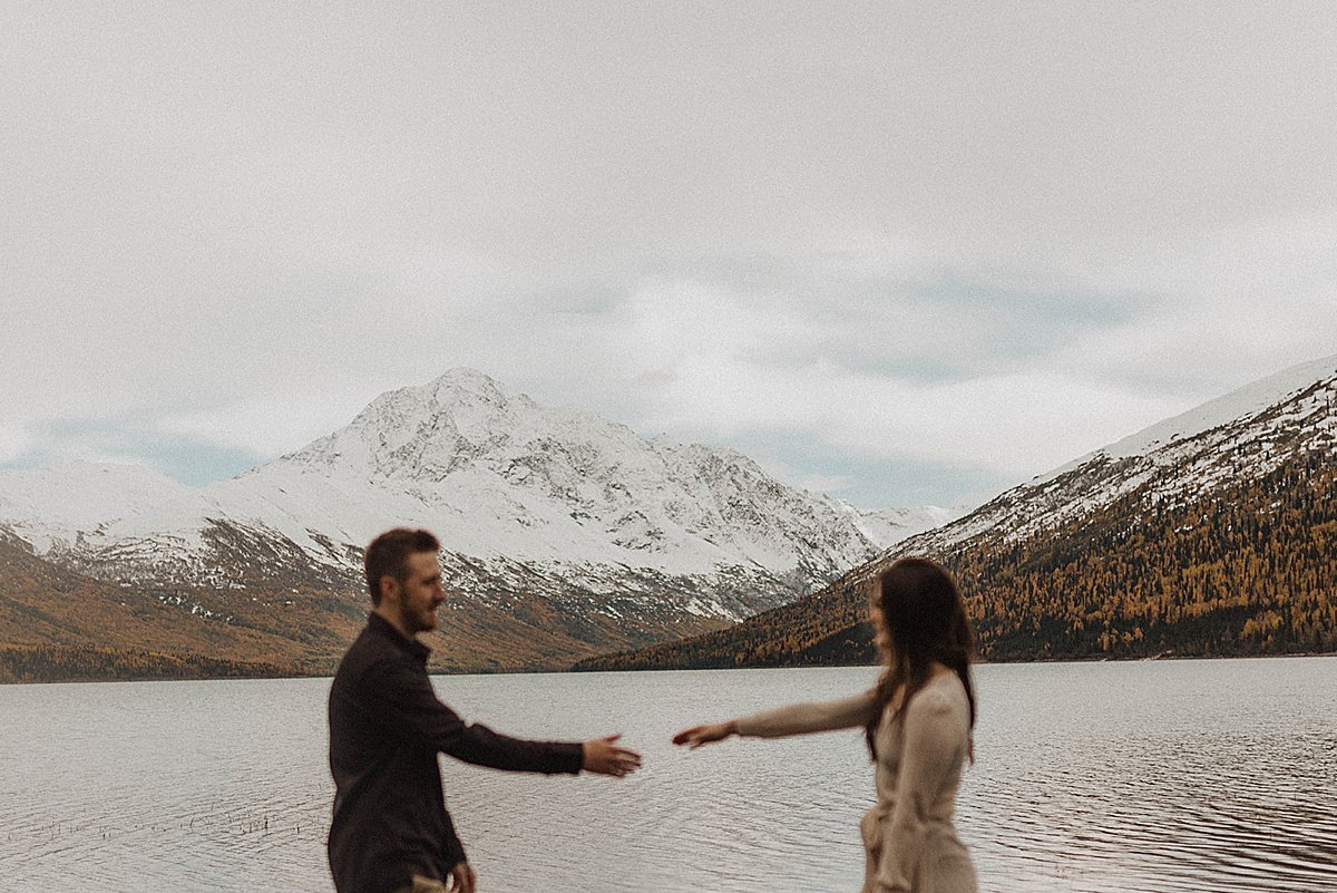  artsy out of focus shot of newly engaged couple in front of snowy mountain lake during autumn engagement shoot 