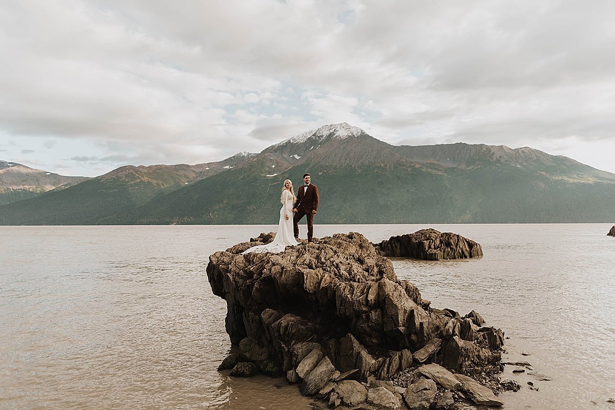  Bride and groom pose on dramatic rock formation in mountain lake after ceremony shot by alaska wedding photographer 