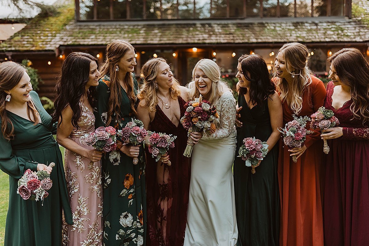  Bridal party in jewel toned velvet gowns laugh holding bouquets with bride before moody glacier creek wedding 