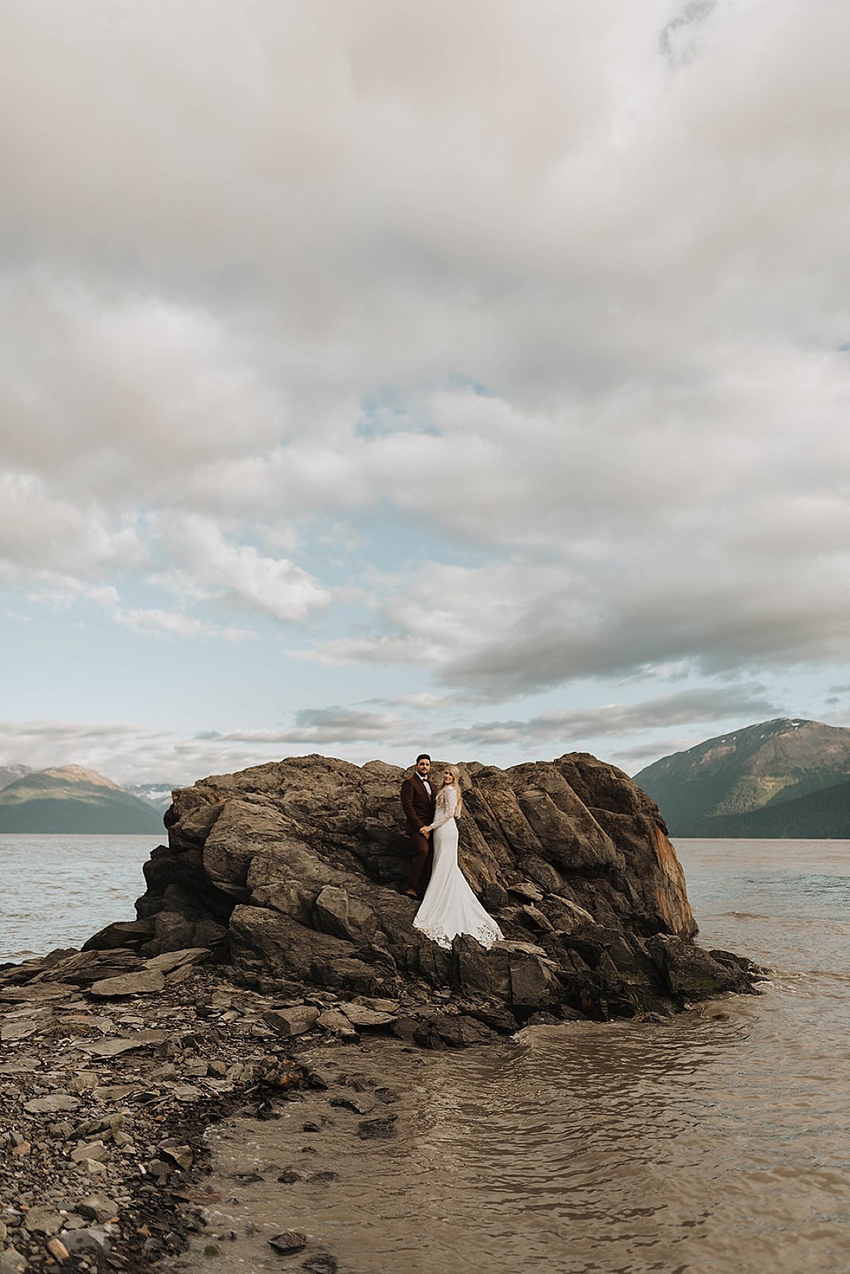  just-married bride and groom pose in dramatic rocky outcrop at mountain lake after moody glacier creek wedding 