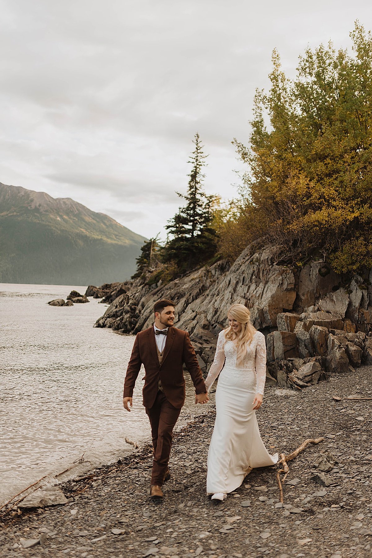  bride and groom take a post-ceremony stroll on rocky, mountain lake beach at alaska wedding shot by Theresa mcdonald photography 