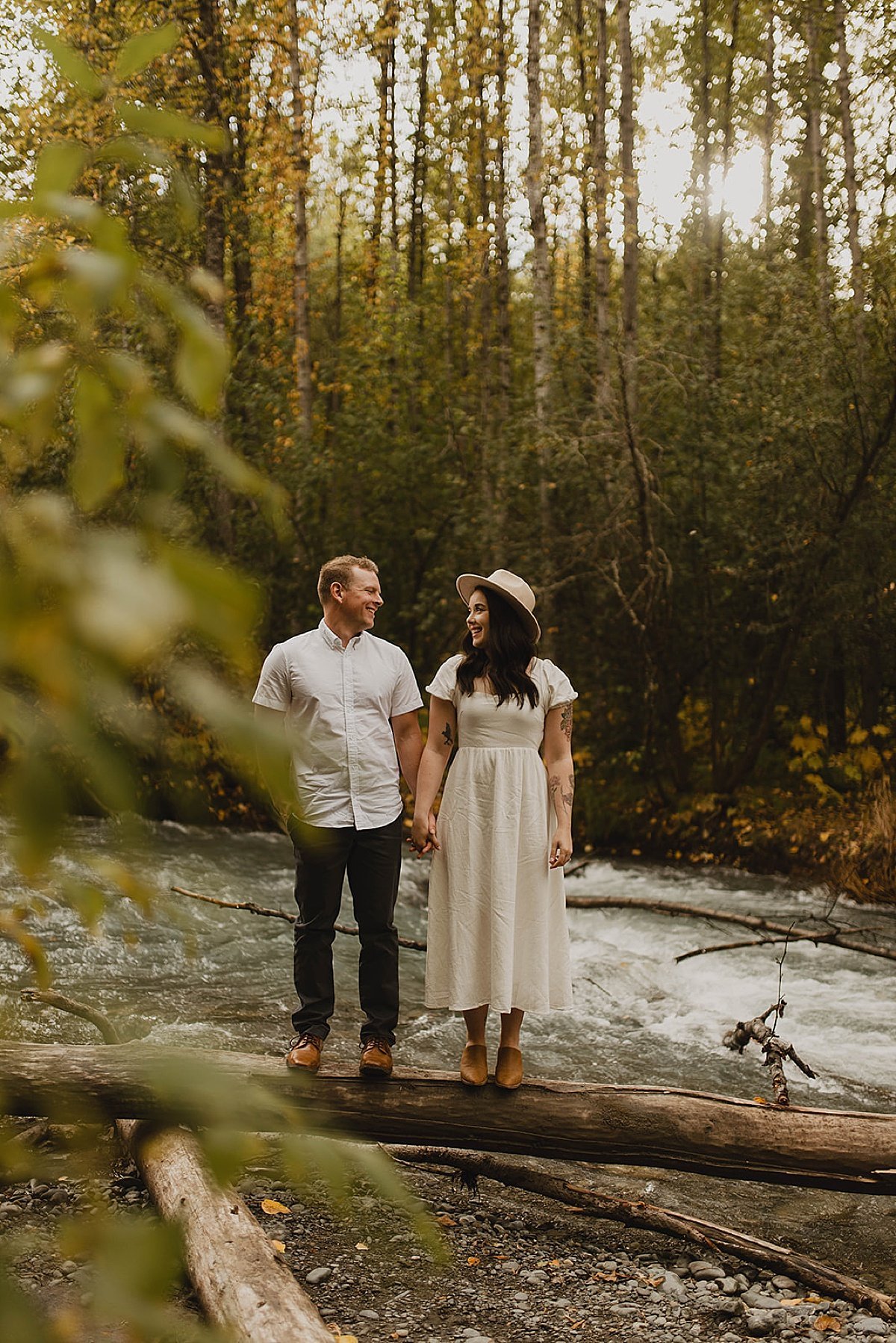  Couple smile at each other through leaves in forest engagement shoot by alaska wedding photographer  