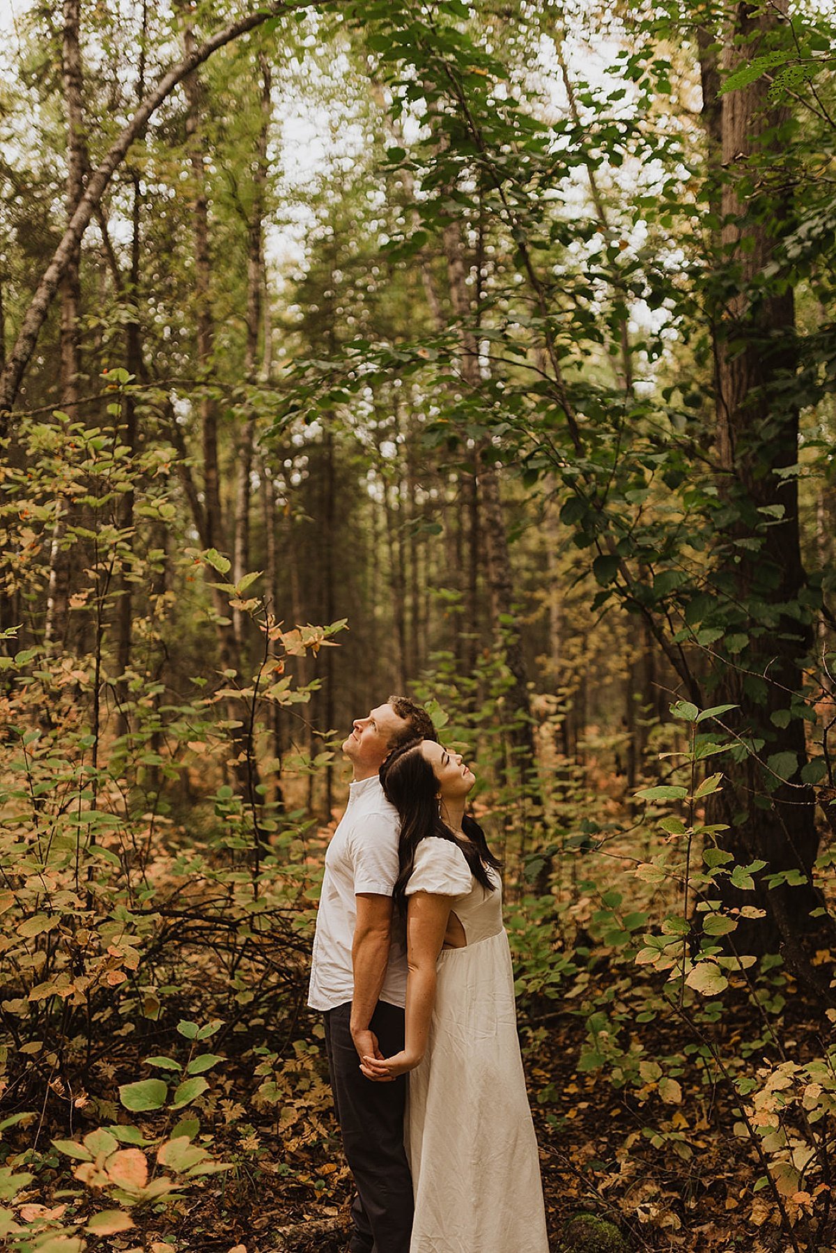  Couple stand back to back in fall leaves during cute engagement shoot 