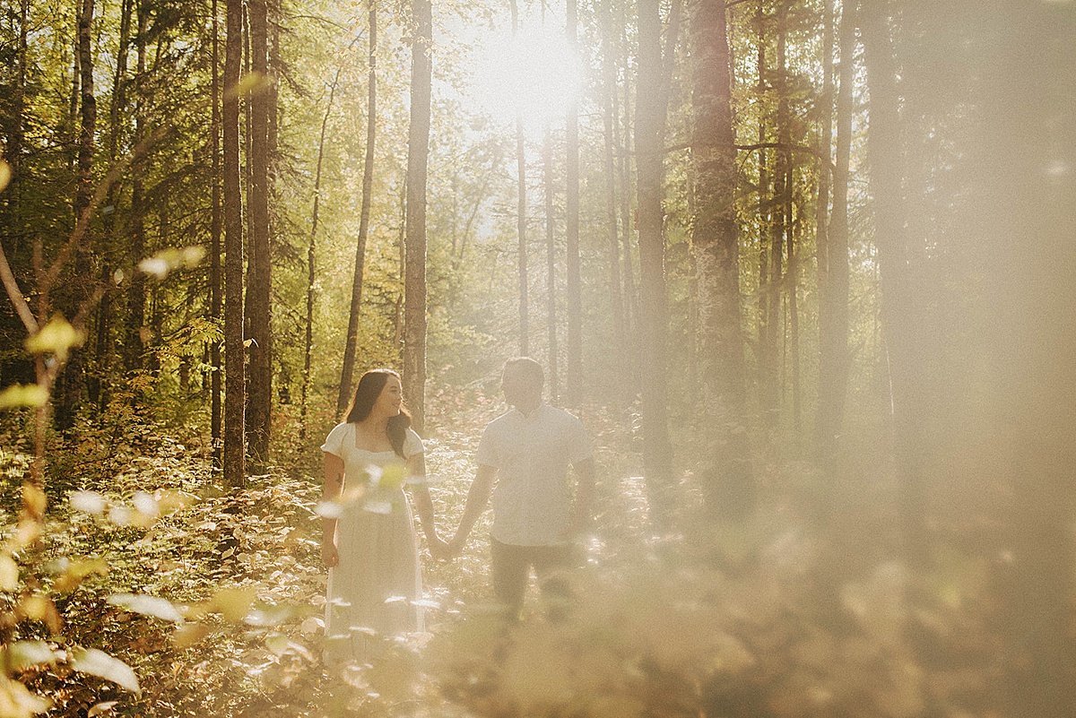  Couple walks through golden mist in a forest for engagement shoot 