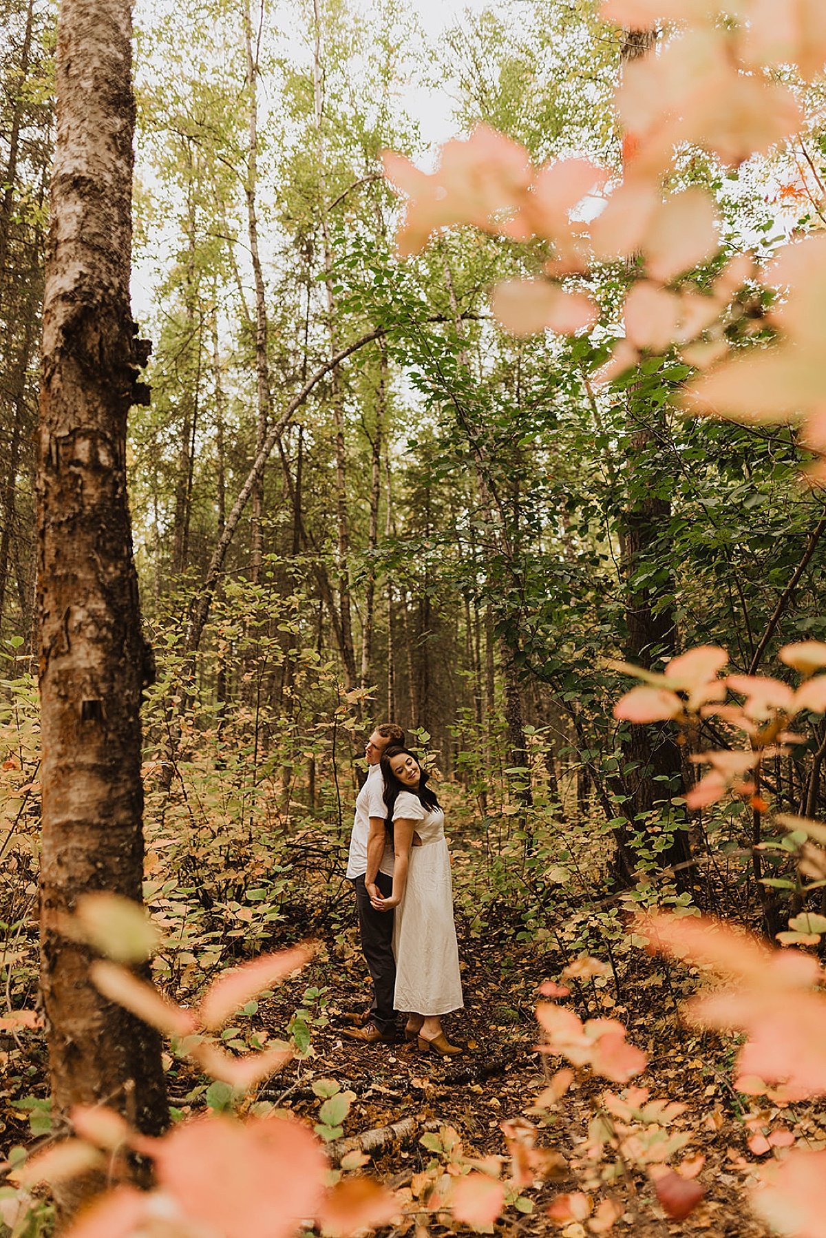  Orange and gold leaves frame a couple holding hands in woodsy engagement shoot. 