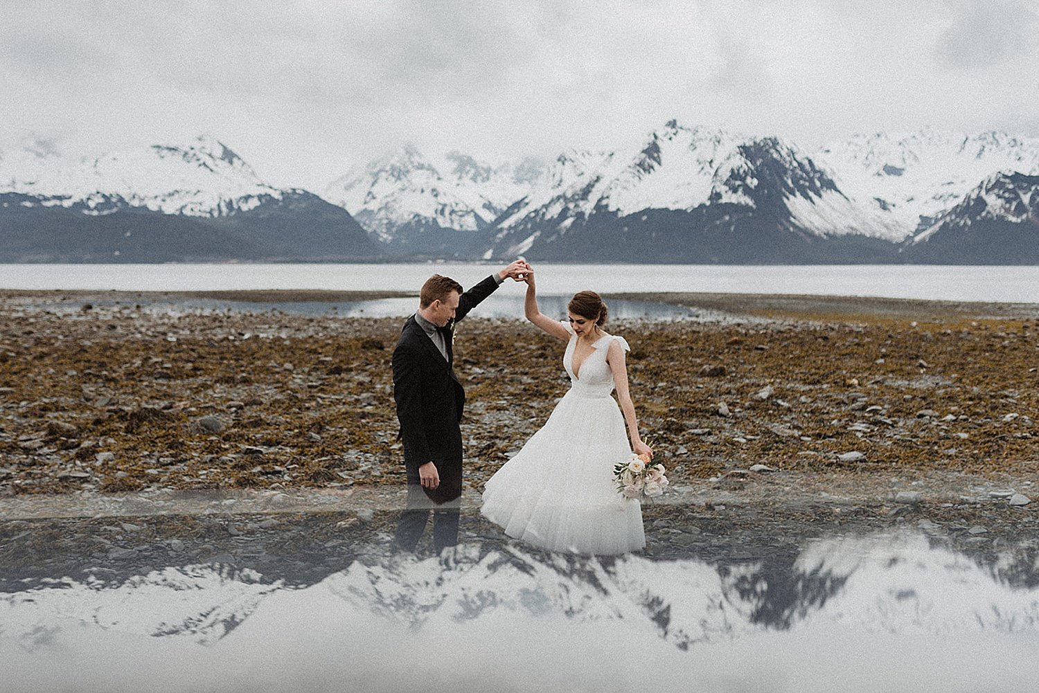  Bride in wedding dress and groom twirling in front of mountain view in alaska vintage inspired shoot 
