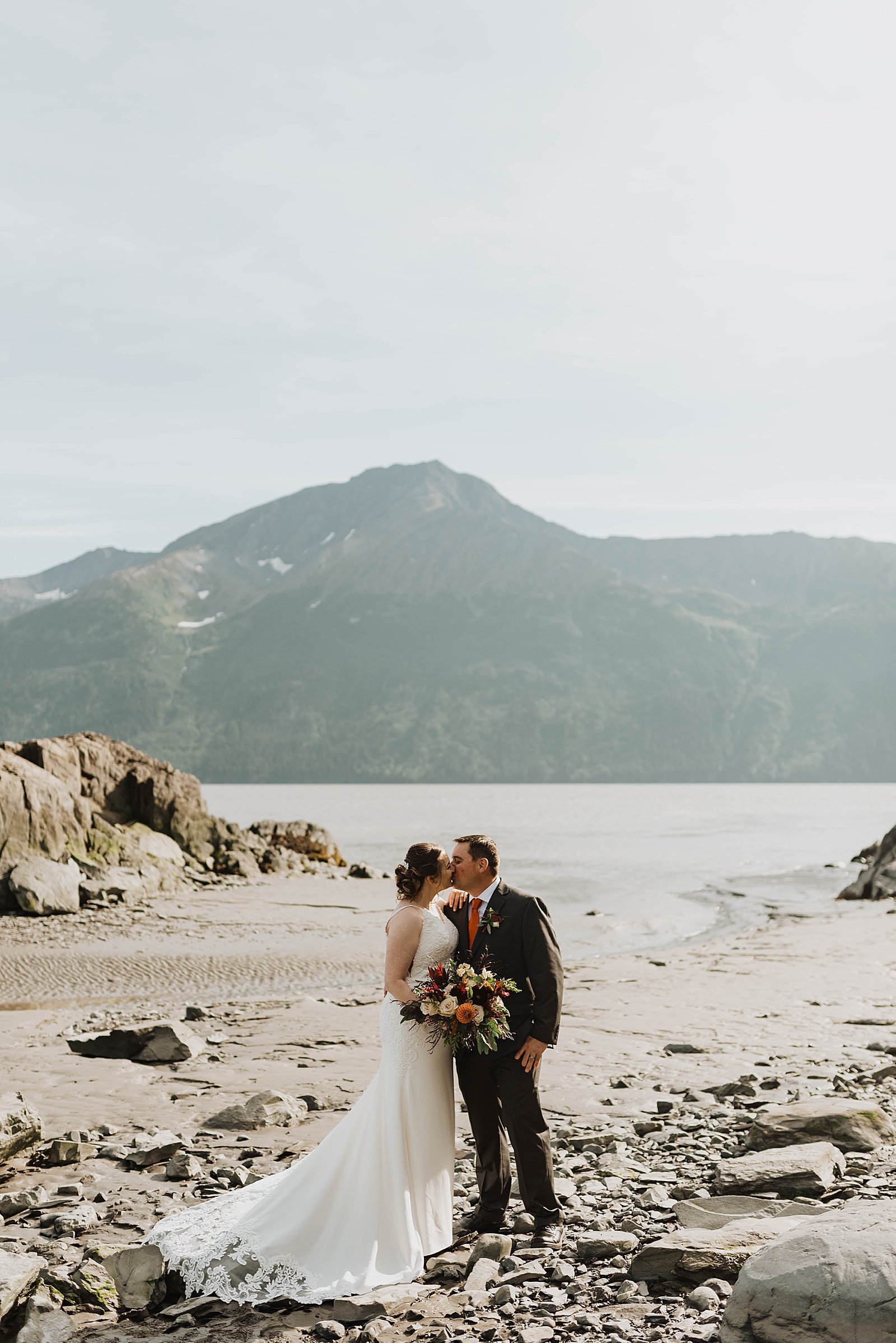  Bride and groom kissing with a large mountain and lake behind them  