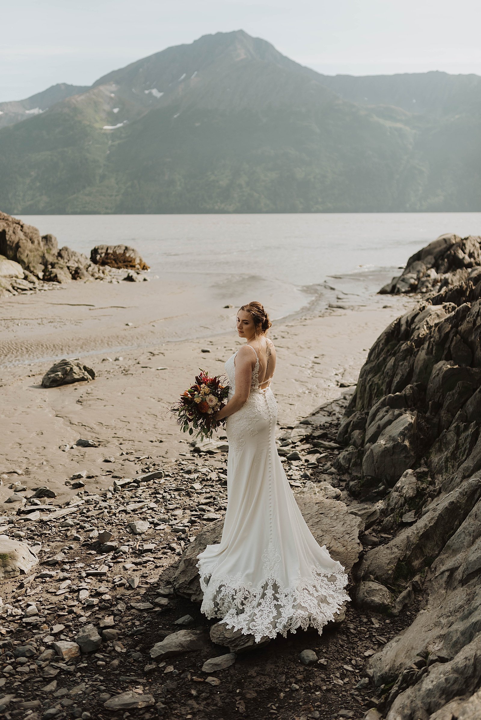  Bride standing on the shore of a lake in Alaska in the Summer  
