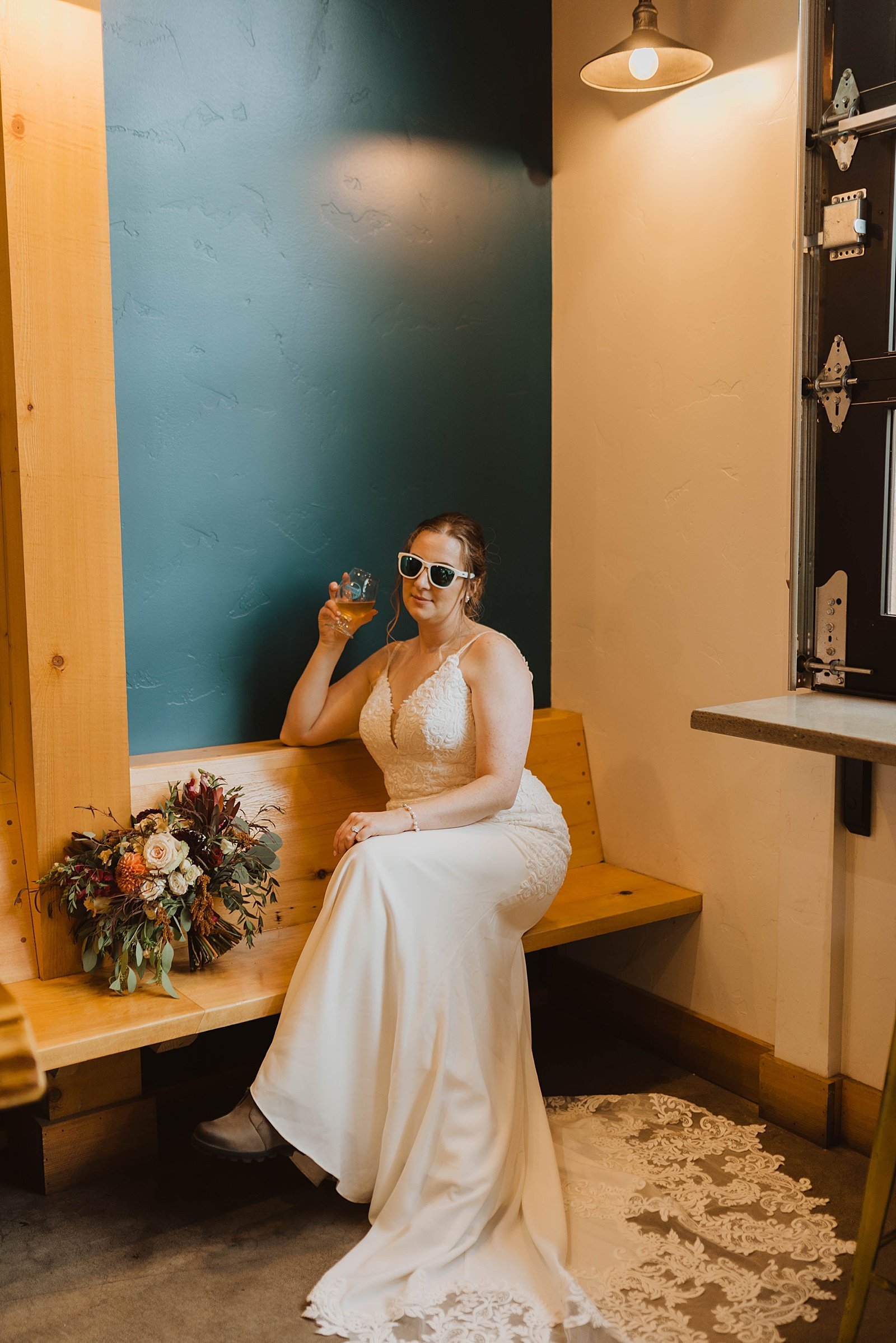  Bride sitting on a bench at a brewery with sunglasses on  