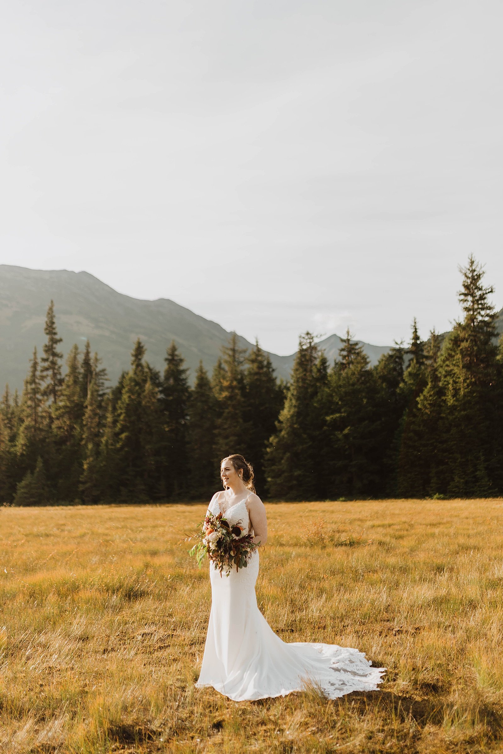  Summer bride in a field with mountains behind her 