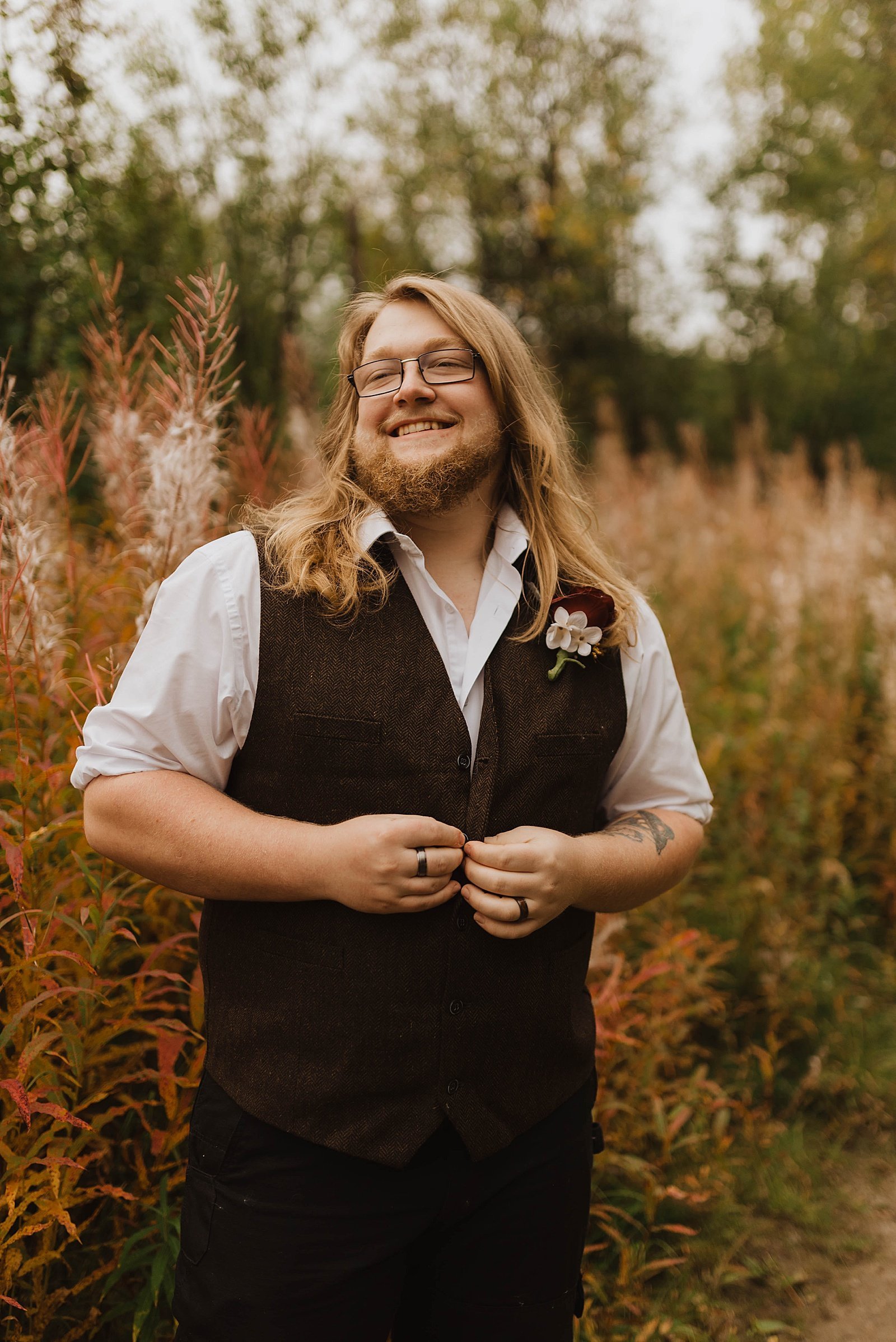  Groom in maroon vest standing in tall grass by Alaska wedding photographer, Theresa McDonald 