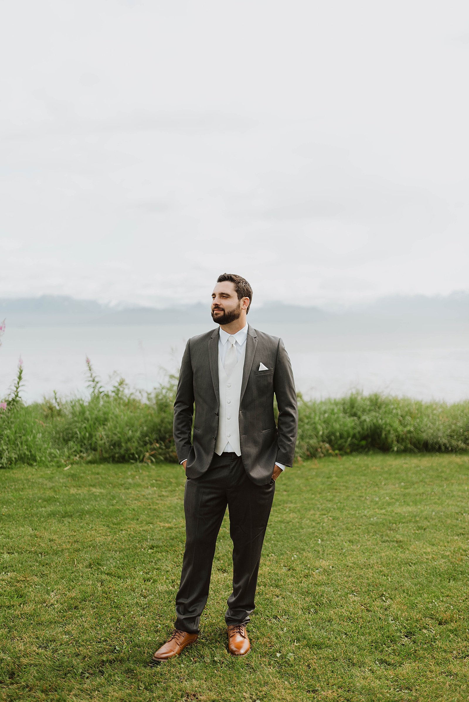  Groom standing on a lawn in front of the water in Homer, Alaska  