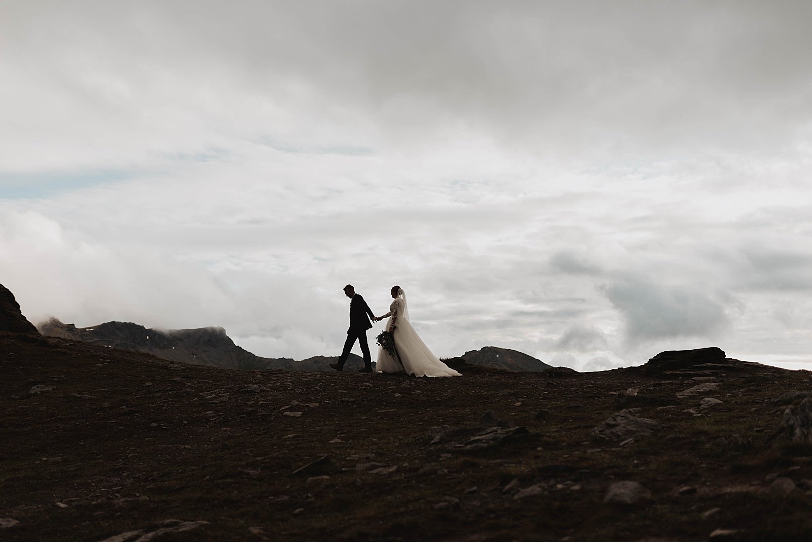  Newlyweds in wedding clothes walking along a ridge at Hatcher Pass.  
