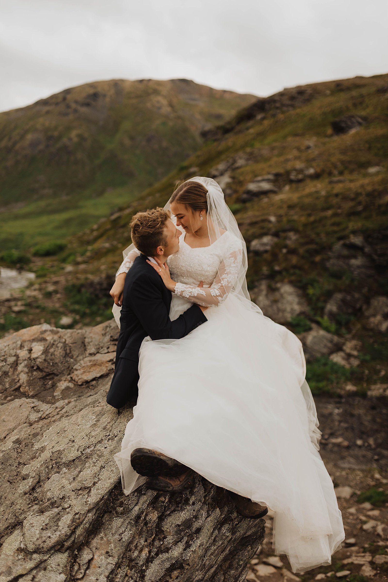  Bride sitting on groom’s lap on a mountain near Anchorage for a bridal session  