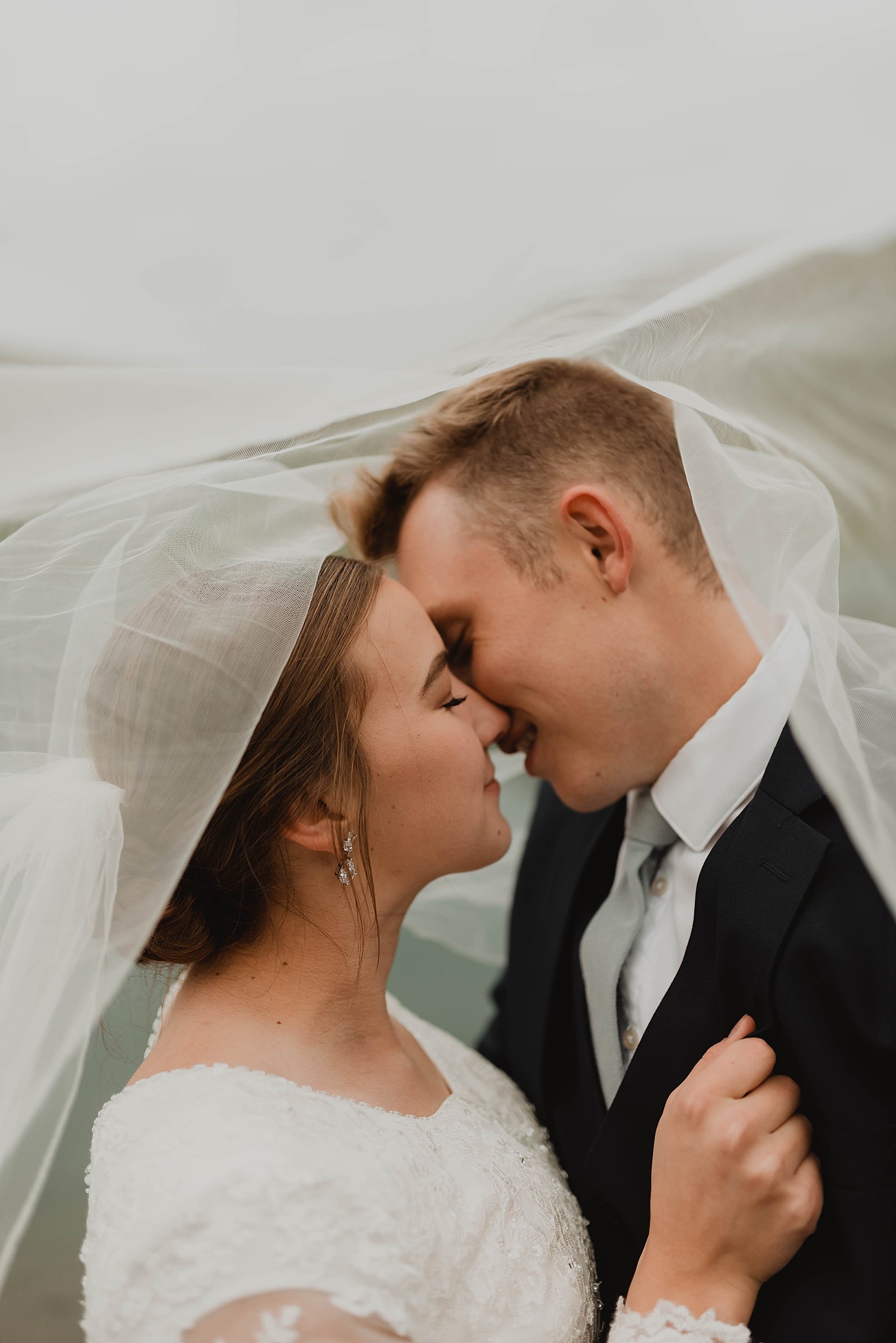  Newlyweds kissing under a veil for a couples adventure session  
