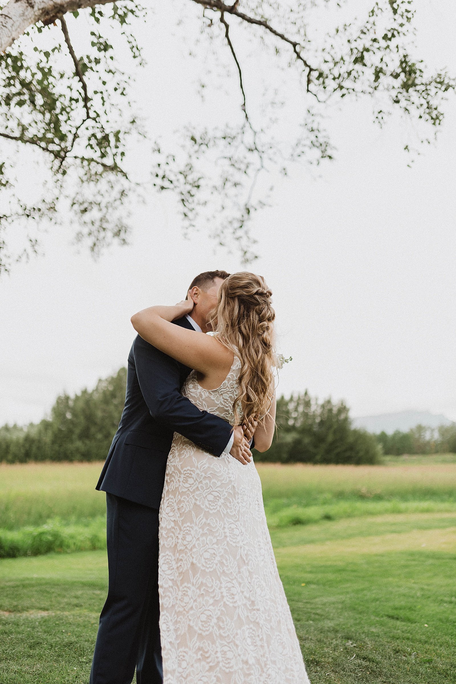  Groom hugging a bride a lace dress  in a field before their ceremony.  