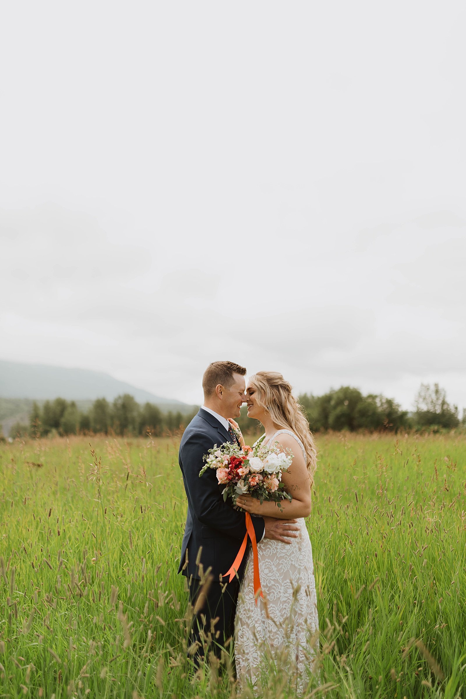  Boho bride &amp; groom standing in a field with the Alaska mountains in the background.  