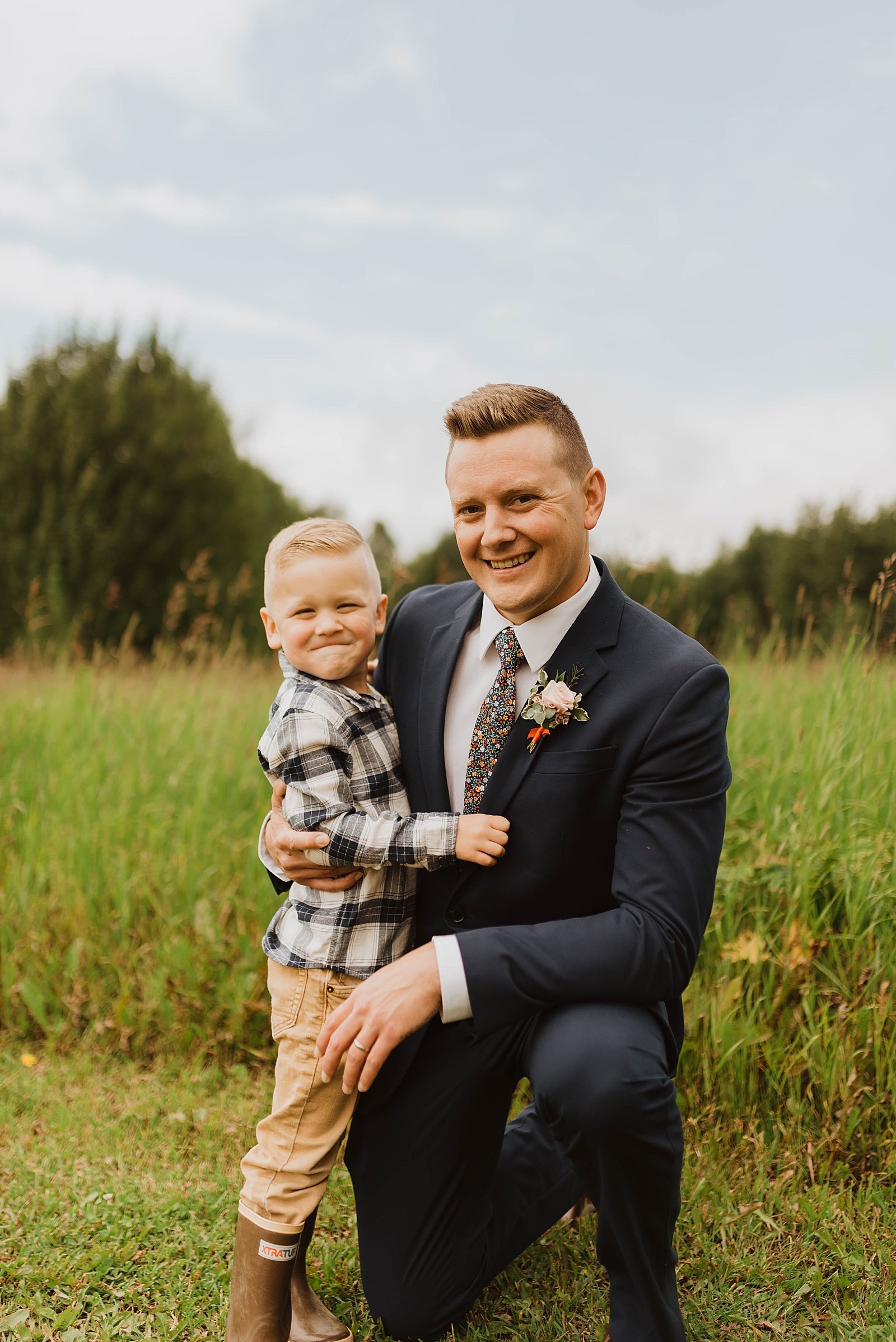  Groom holding son in a plaid shirt on his knee after a family vow renewal in Anchorage.  