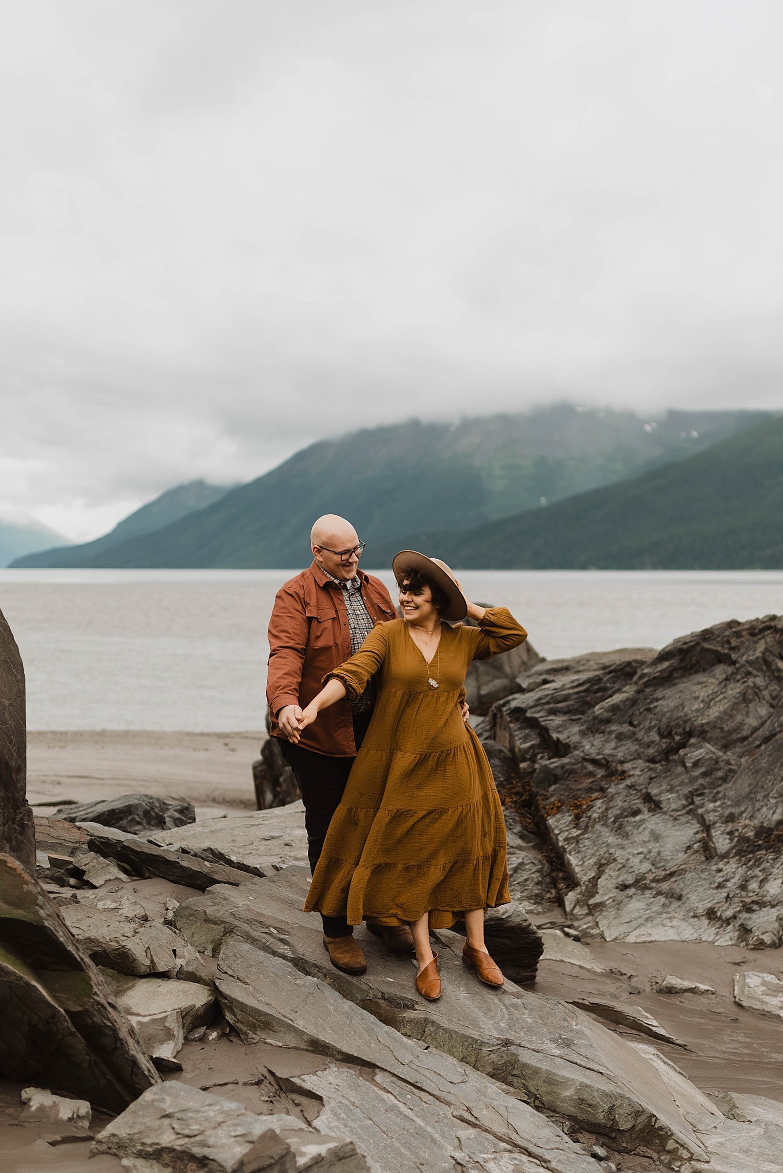 Man and woman standing on the shore of a lake for their romantic anniversary session in Alaska.