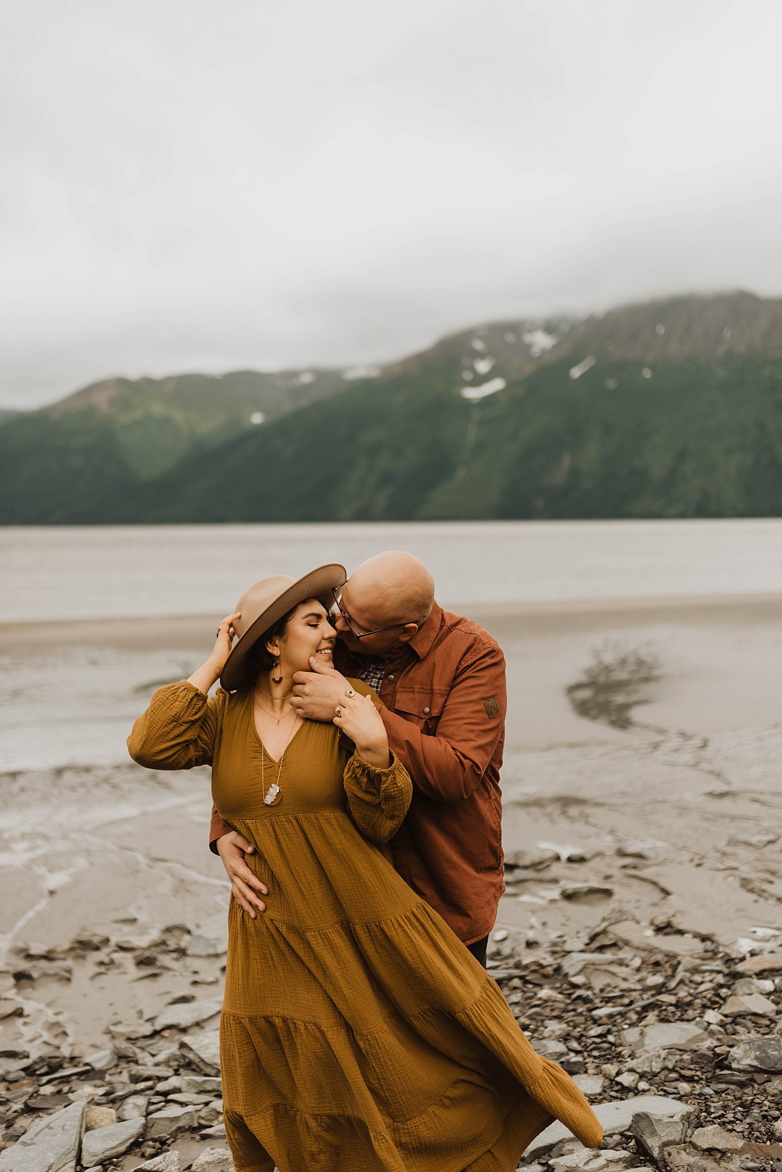  Woman in long orange dress and man in rust shirt kissing for their romantic anniversary session 