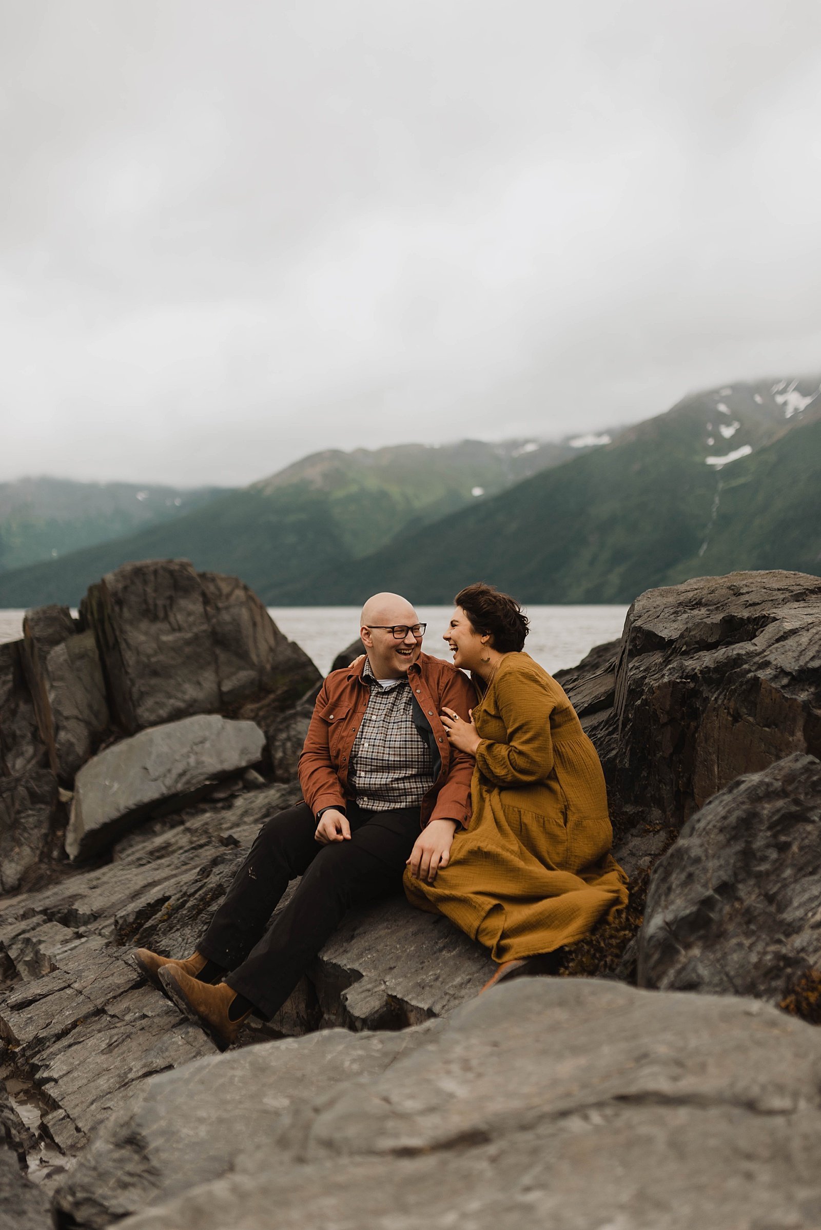  Man and woman sitting on a rock together with mountains in the background for their romantic anniversary session. 
