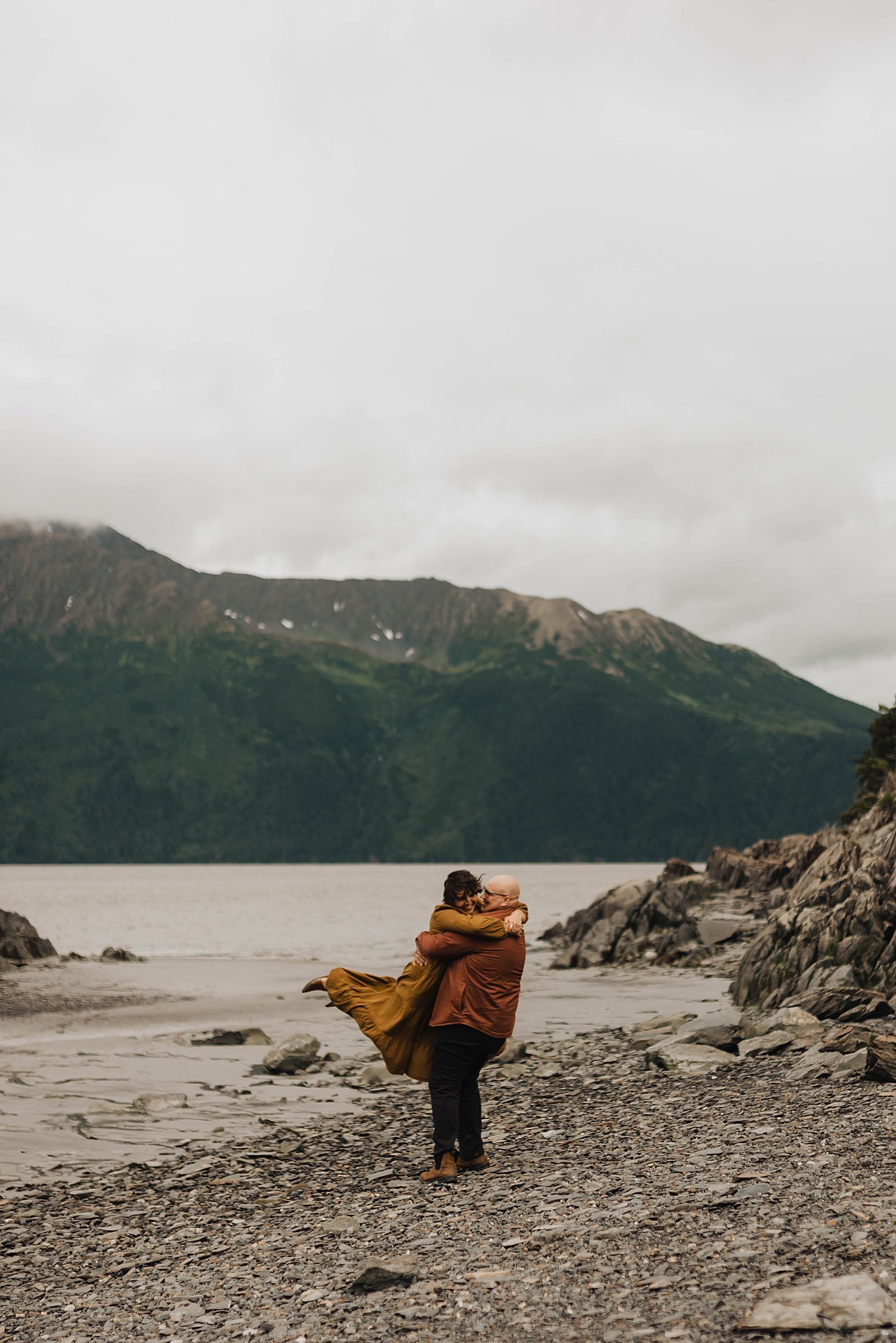  Man spins around his wife with a lake and Alaska mountains in the background.  