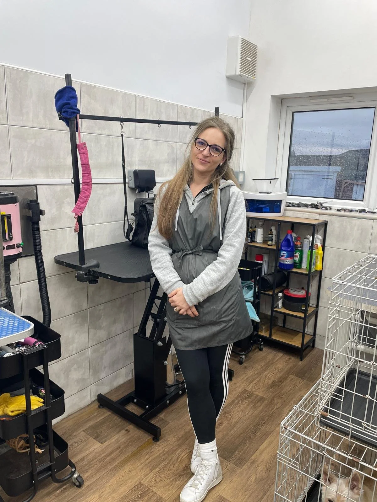 Person standing in a pet grooming salon with grooming tables and equipment in the background.