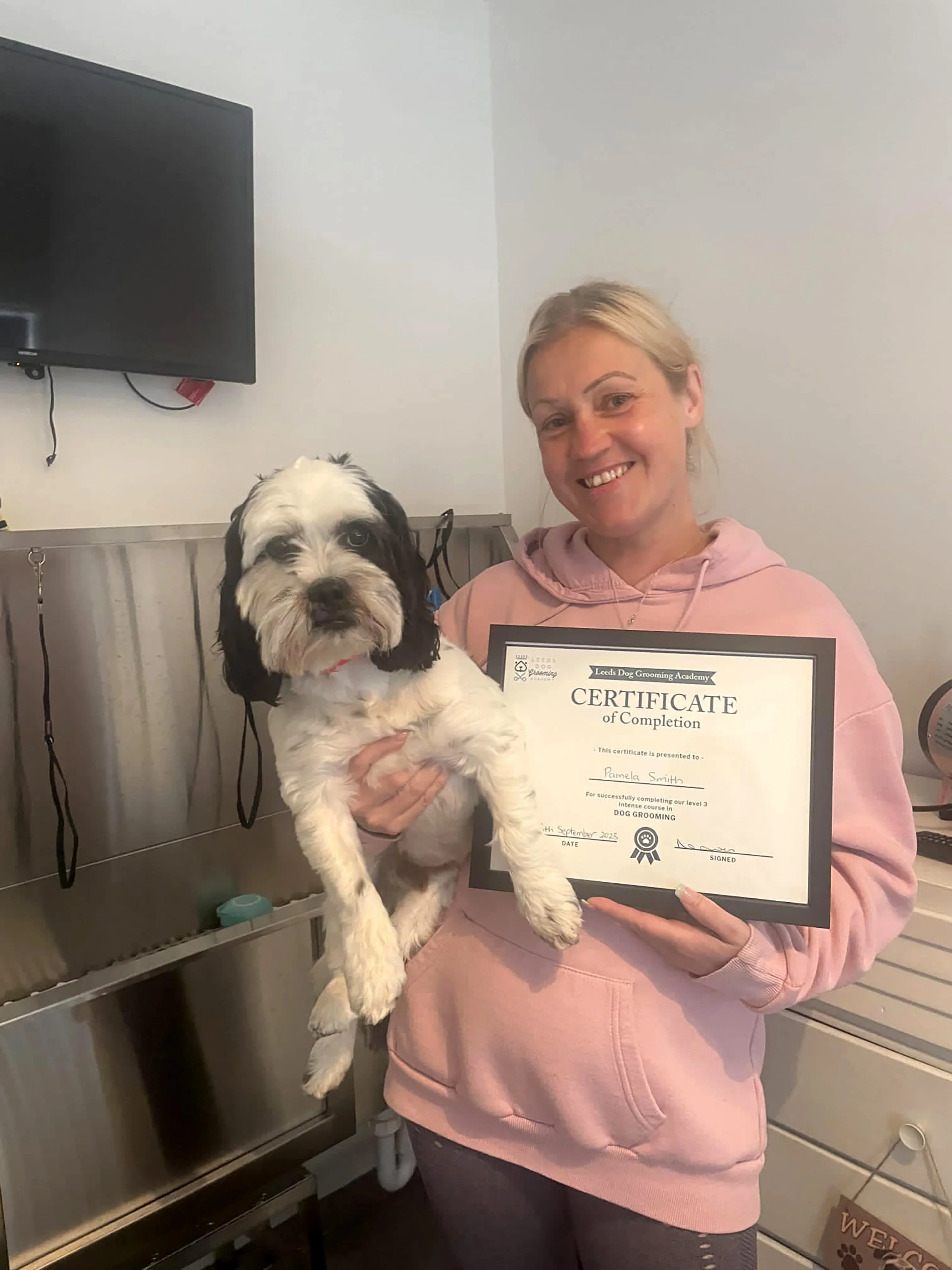 Woman holding a dog and a certificate in a room with grooming equipment.