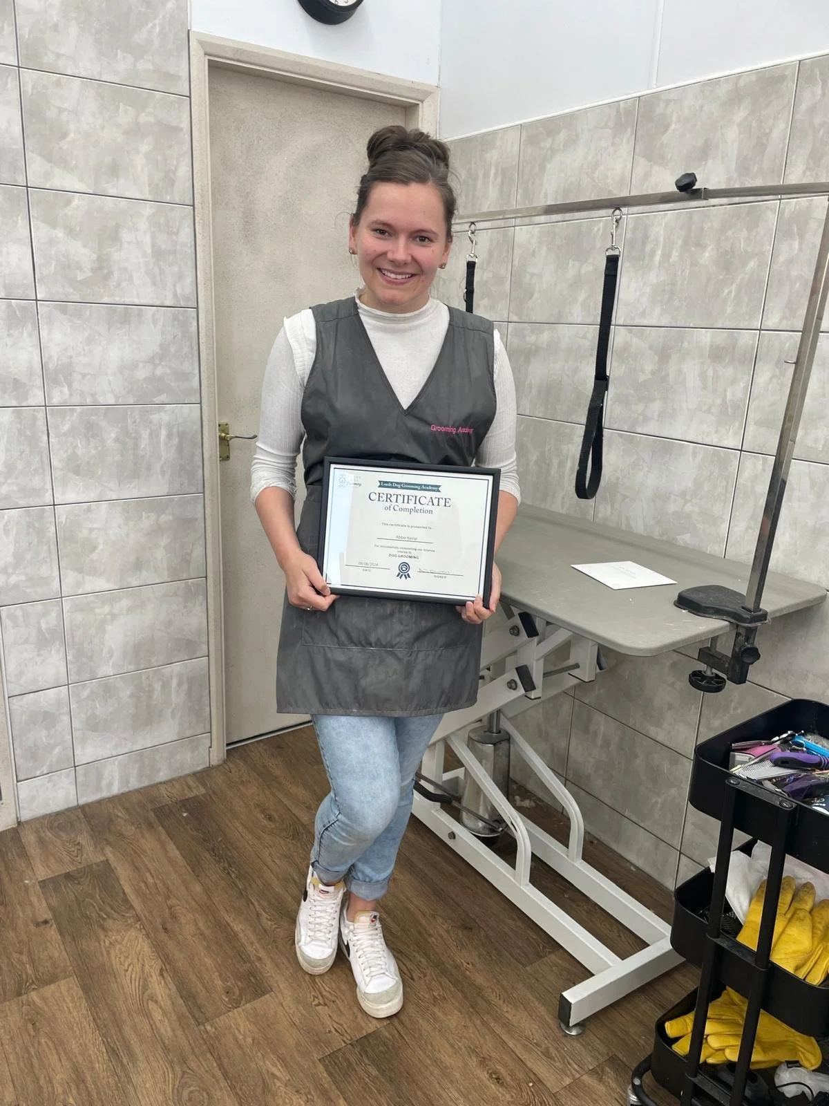 Person holding certificate in pet grooming salon, standing near grooming table and tools.