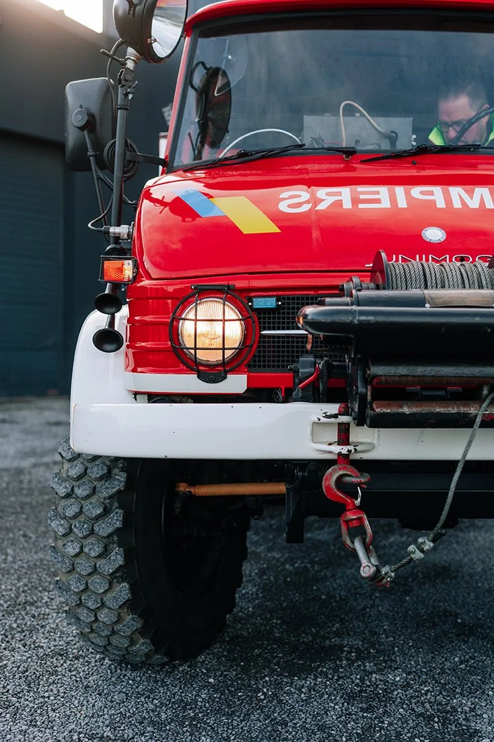 Close-up of a red emergency rescue vehicle with a front headlamp, tire, and equipment bumper, with a person visible inside wearing safety gear.