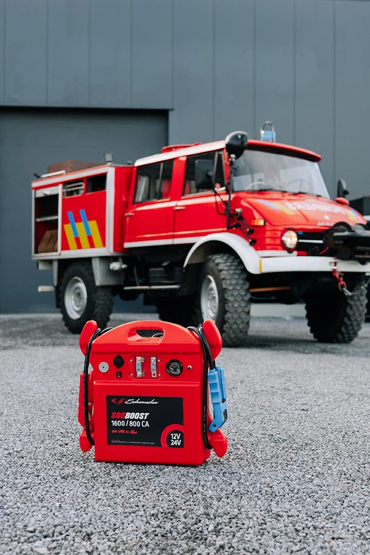 A red fire truck parked outdoors in front of a grey building with a blue door and a red rescue equipment box in the foreground.