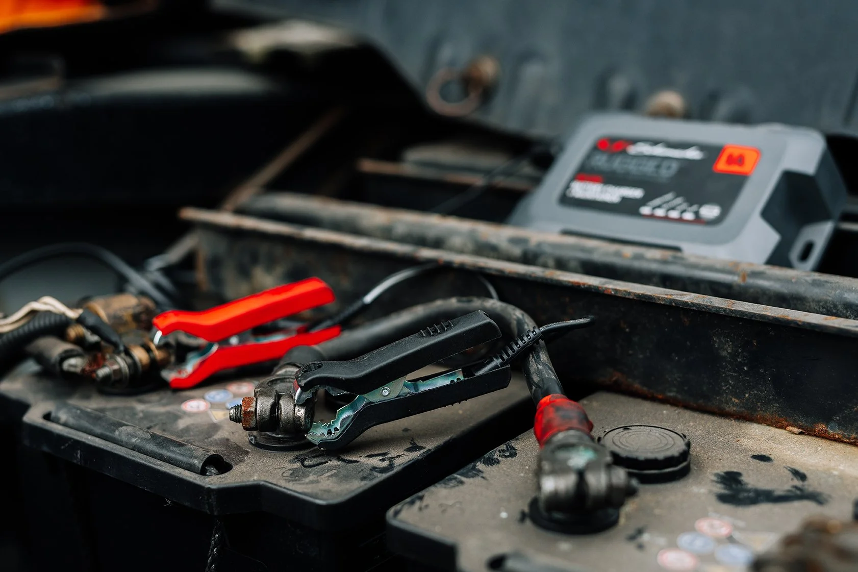 Tools and a battery inside a toolbox with a rusty metal exterior.