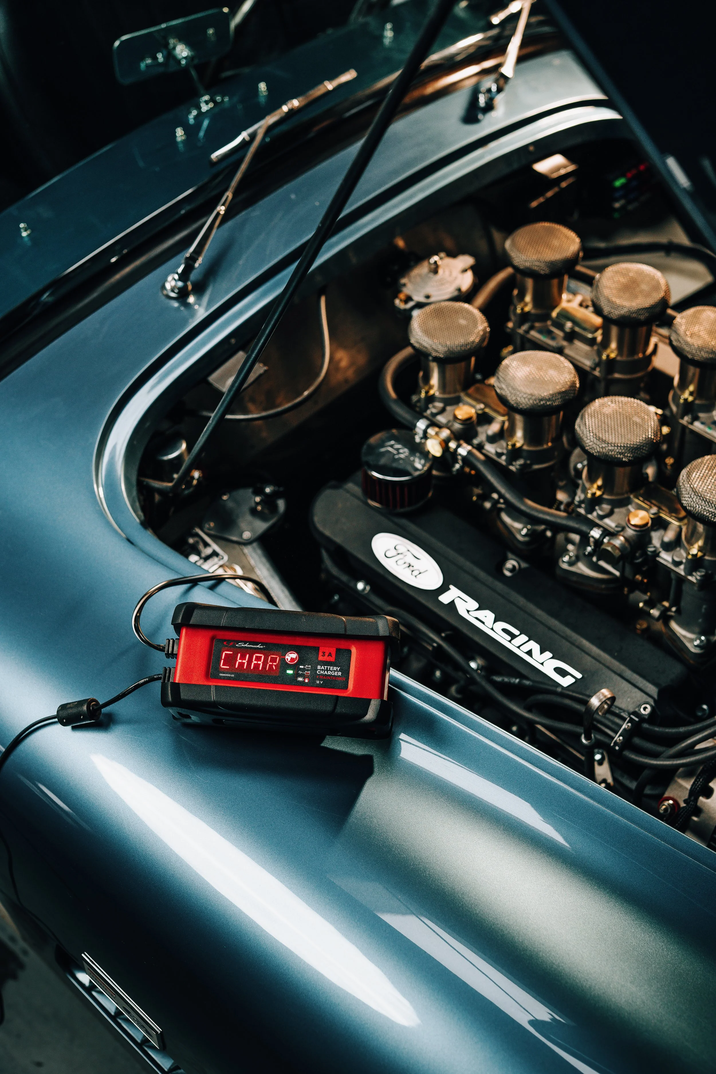 Close-up of a vintage racing car engine with a digital charger displaying 'CHAR' in the foreground.