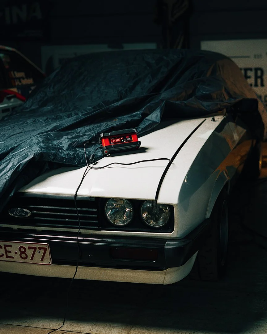 A white vintage Ford car with a black tarp covering part of it, parked inside a garage. A diagnostic scanner is connected to the car, displaying the message 'CHAR'.