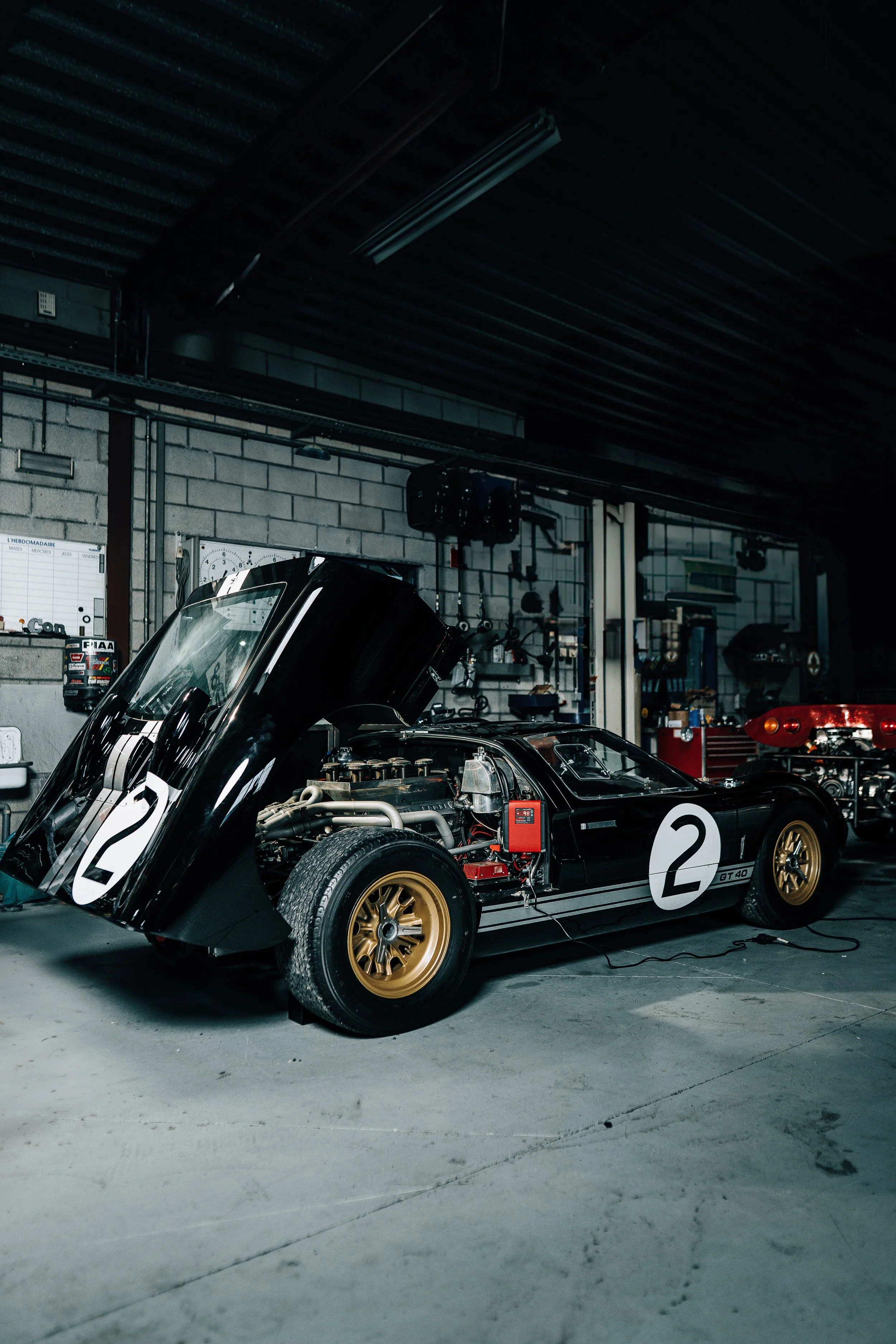 A vintage race car with the number 2 on its side, inside a garage or workshop with tools and equipment hanging on the wall.