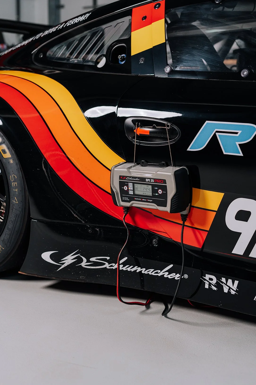 Close-up of a race car with a black, red, and yellow color scheme, with a battery charger attached to its side.