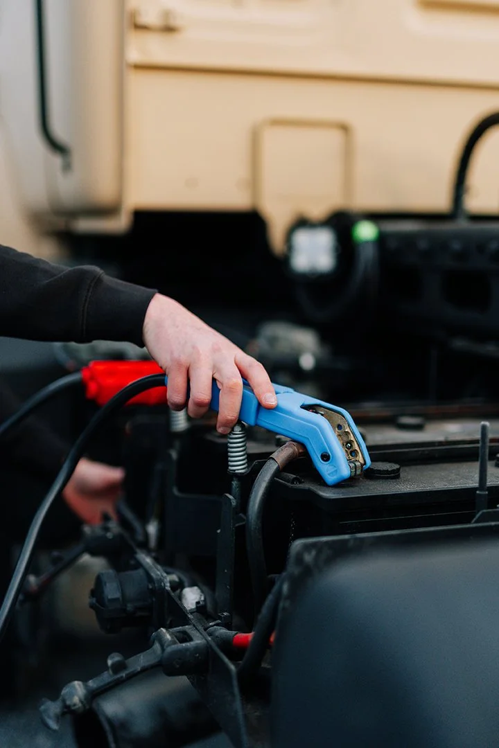 A person using a blue jumper cable to jump-start a vehicle's battery.