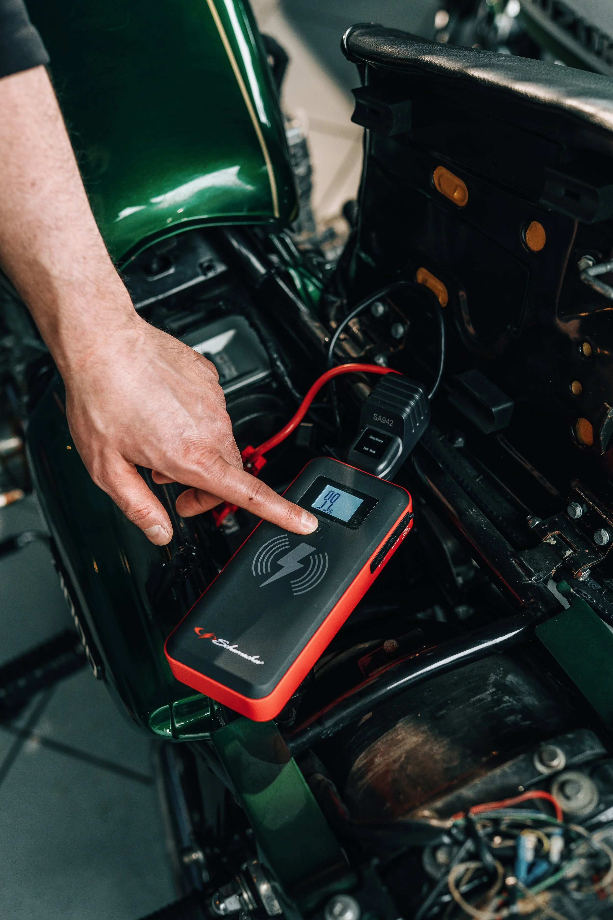 A person's hand operating a digital electrical tester on a motorcycle engine, with electrical wires and components visible.