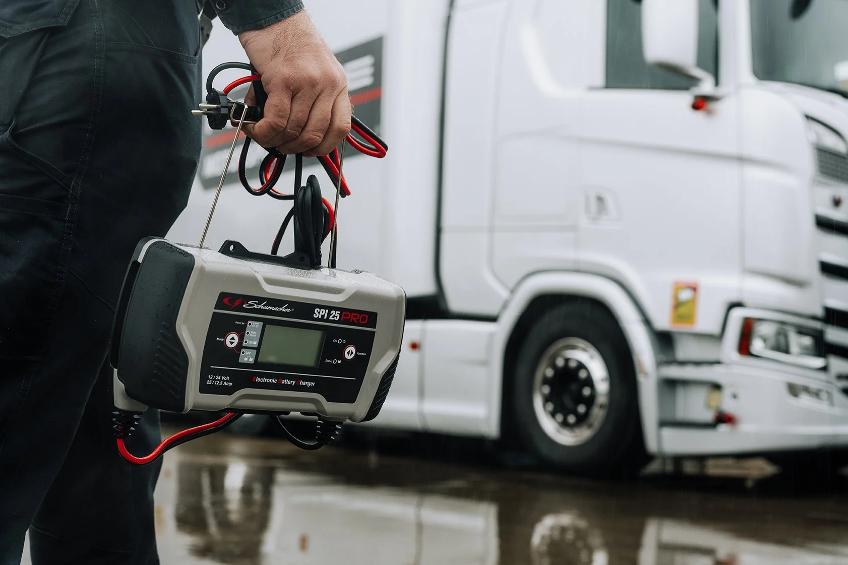 Man holding a battery charger in front of a white semi-truck