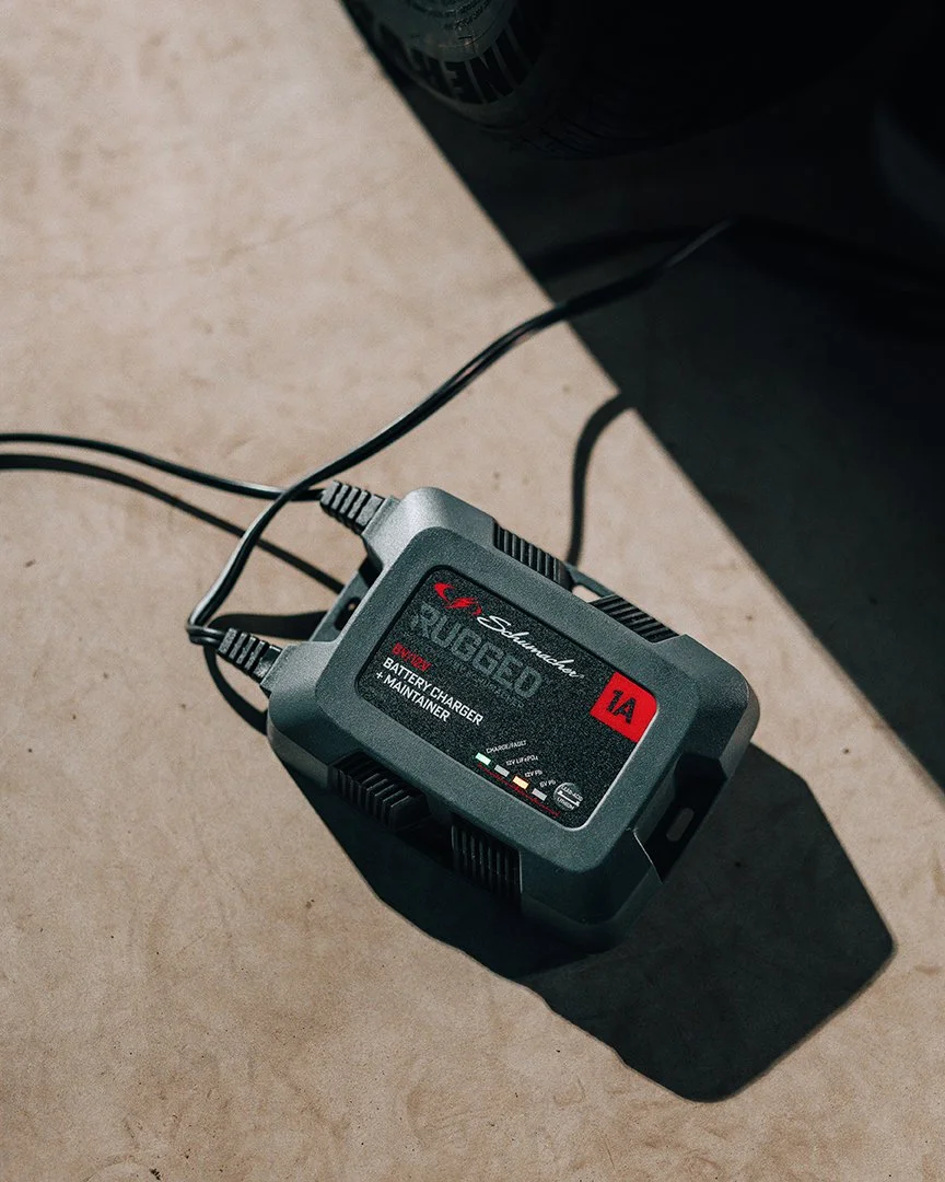 A black battery charger and maintainer with the brand name 'Balmar' and the model number 'SAG31825C' is plugged into an electrical outlet, resting on a beige surface.
