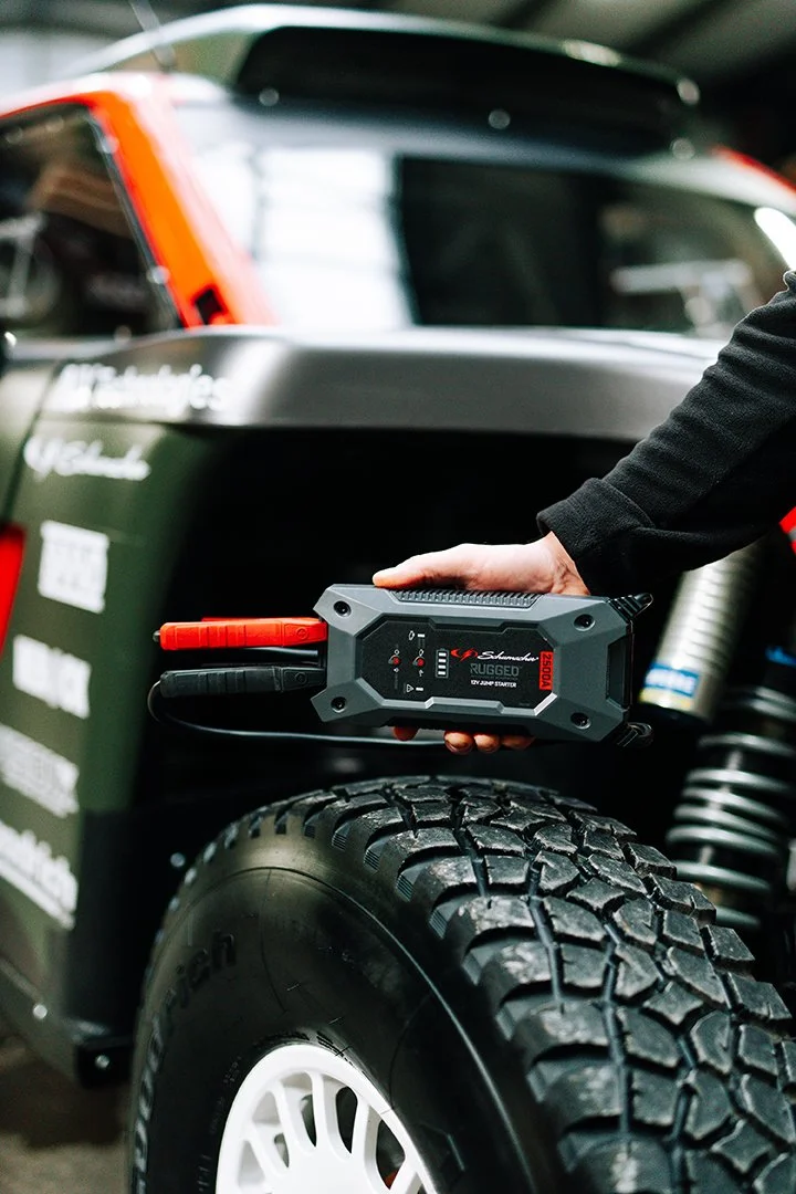A person holding a jump starter connected to a vehicle's battery in a garage or workshop.