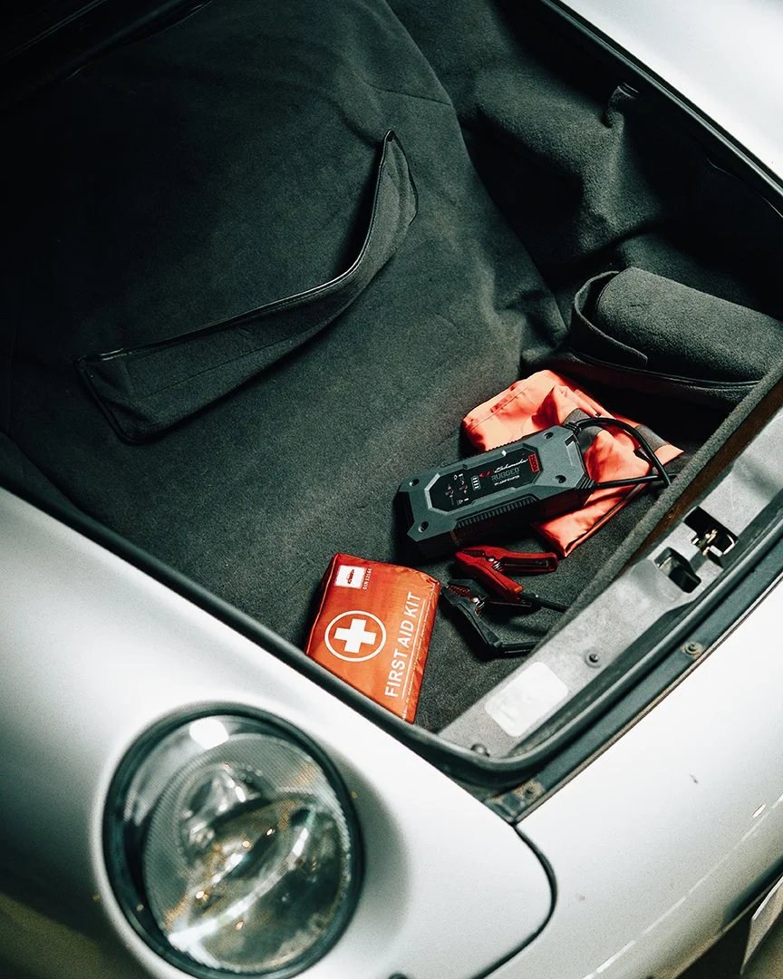 Car trunk with a first aid kit, jumper cables, portable battery charger, and small tool bag.