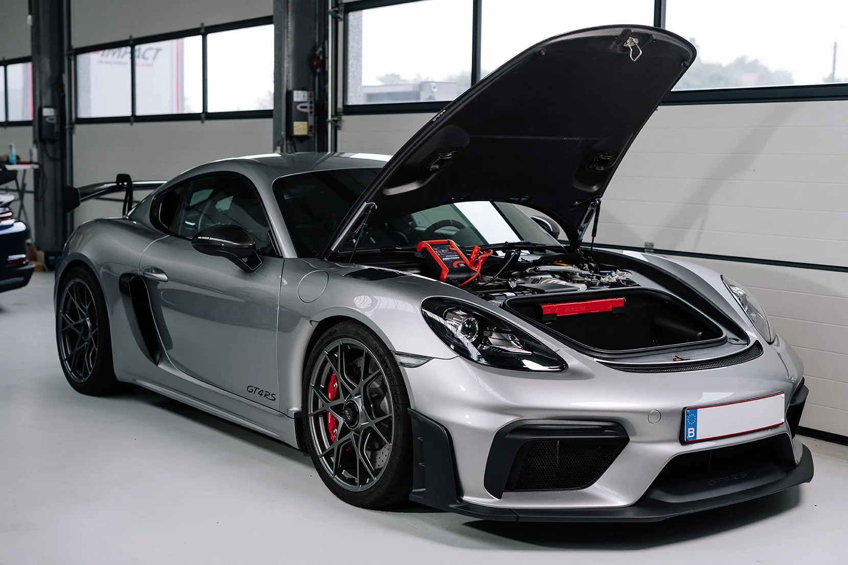 Silver sports car with open front hood inside a garage, with battery testing equipment placed on the engine bay.